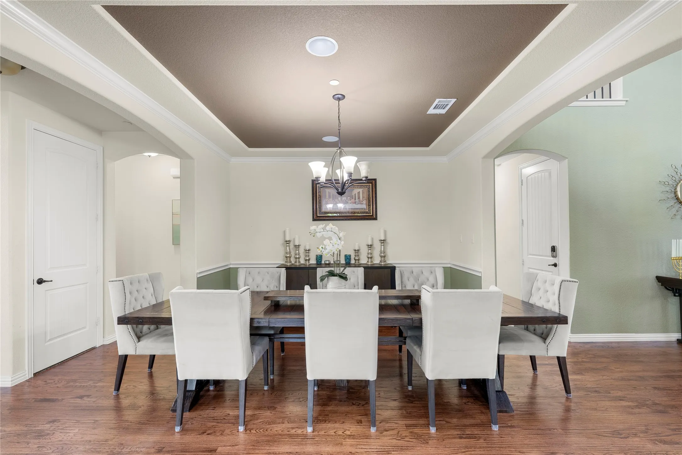 Recessed ceiling with a contrasting painted inset, crown molding, wood-finish flooring, and arched doorways