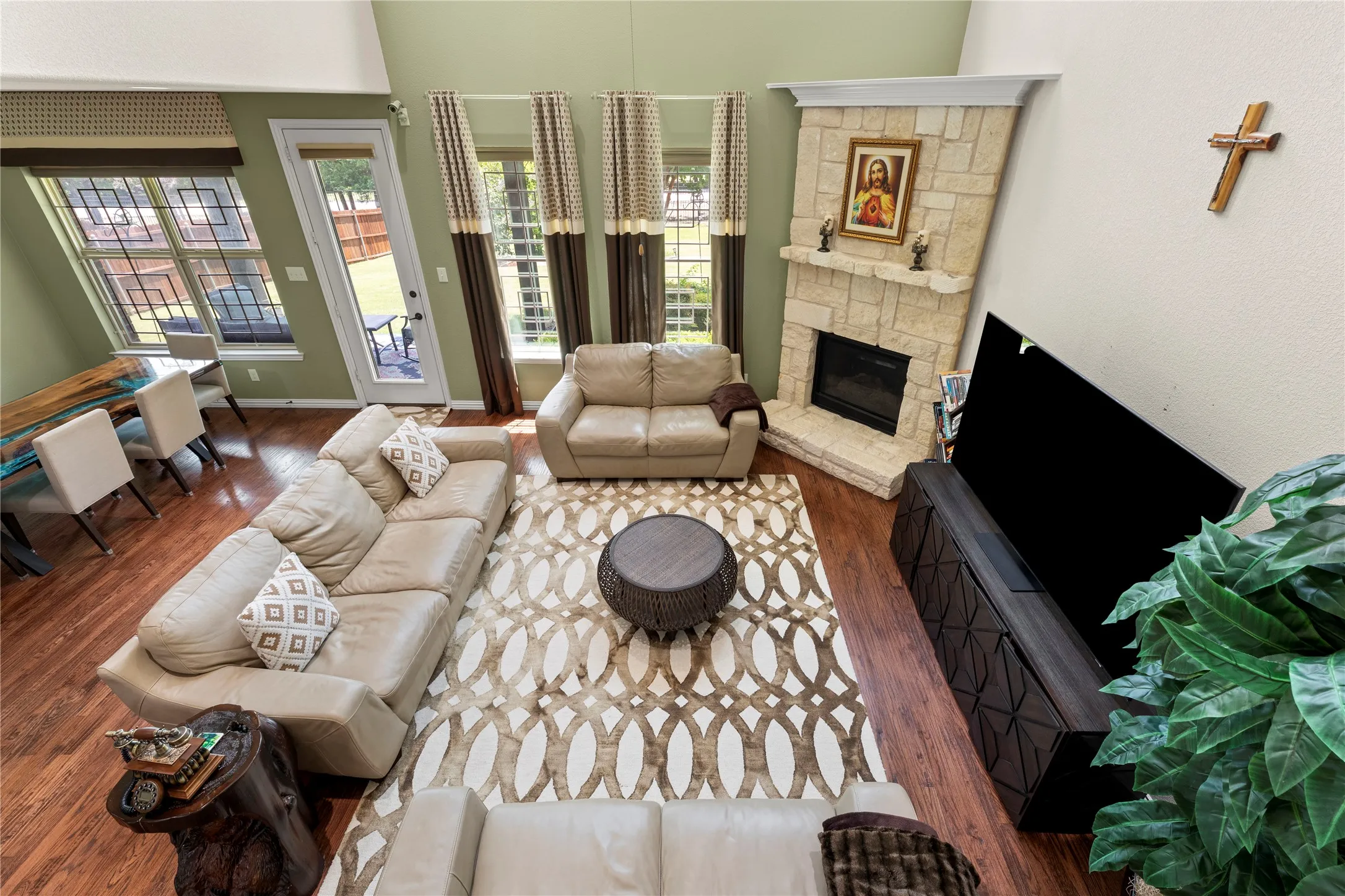 Vaulted living area featuring wood-finish flooring, a stone-surround fireplace with mantel, and multiple windows