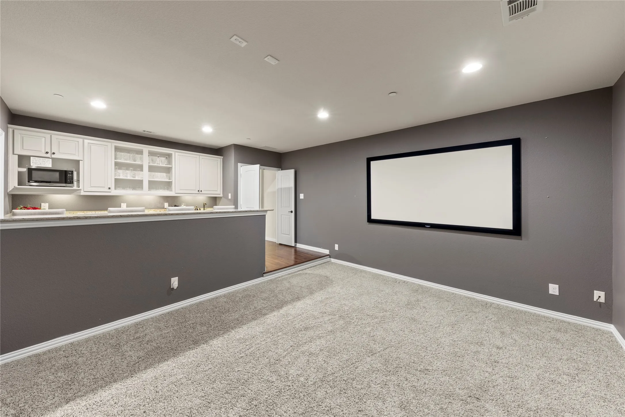 Carpeted entertainment area featuring a built-in projection screen, recessed lighting, and a partial wall