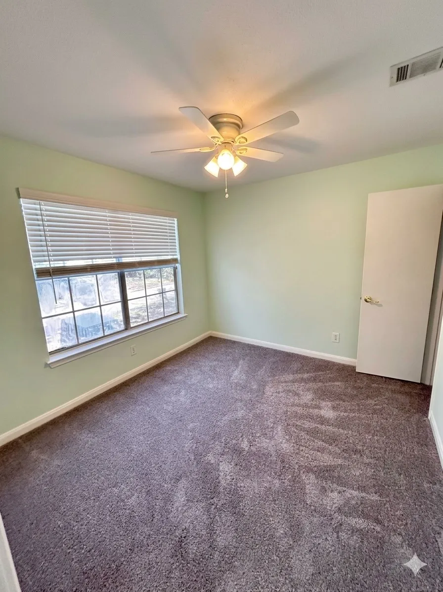 Carpeted room featuring a ceiling fan with integrated lighting, a window with blinds, and a white door with a lever handle