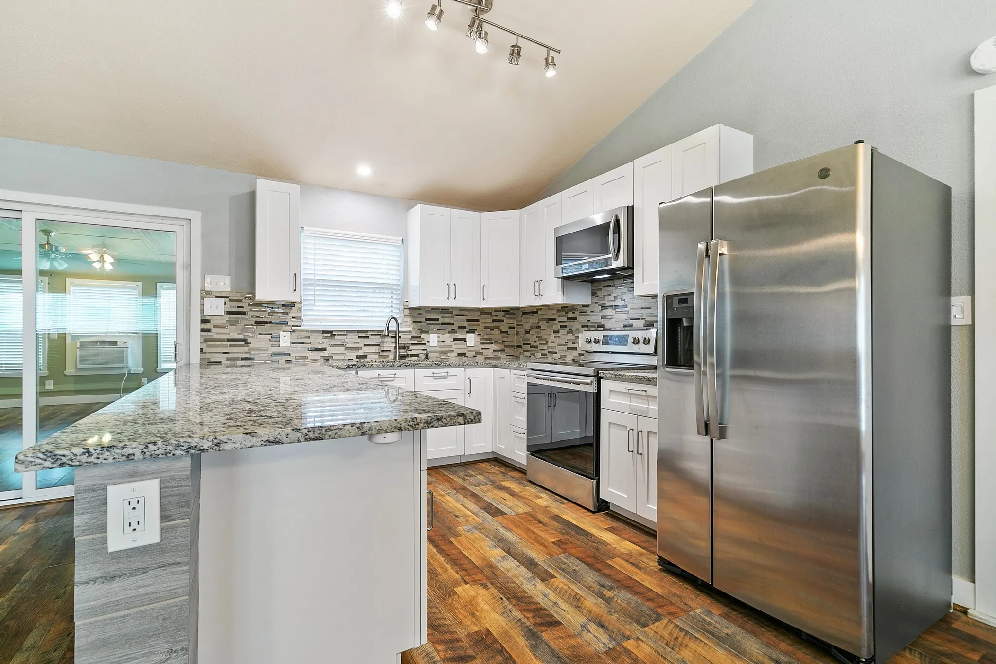 Kitchen featuring wood-finish flooring, white cabinetry, stainless steel appliances, a tile backsplash, and a granite-style countertop