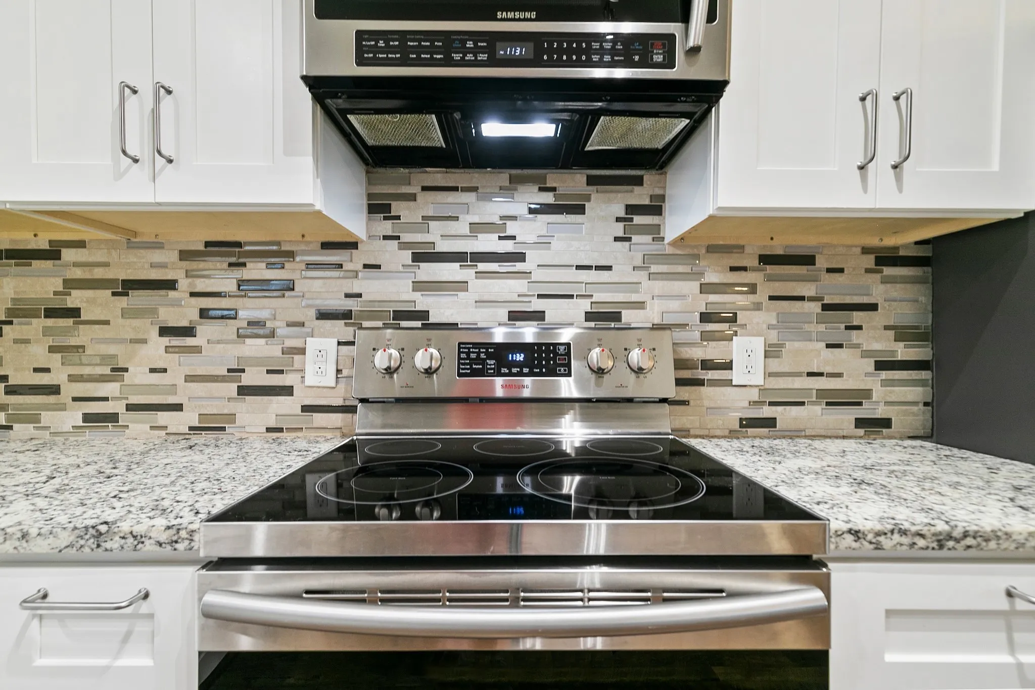 Stainless steel range with a ceramic cooktop, white upper and lower cabinetry, granite countertops, tile backsplash, and a built-in microwave