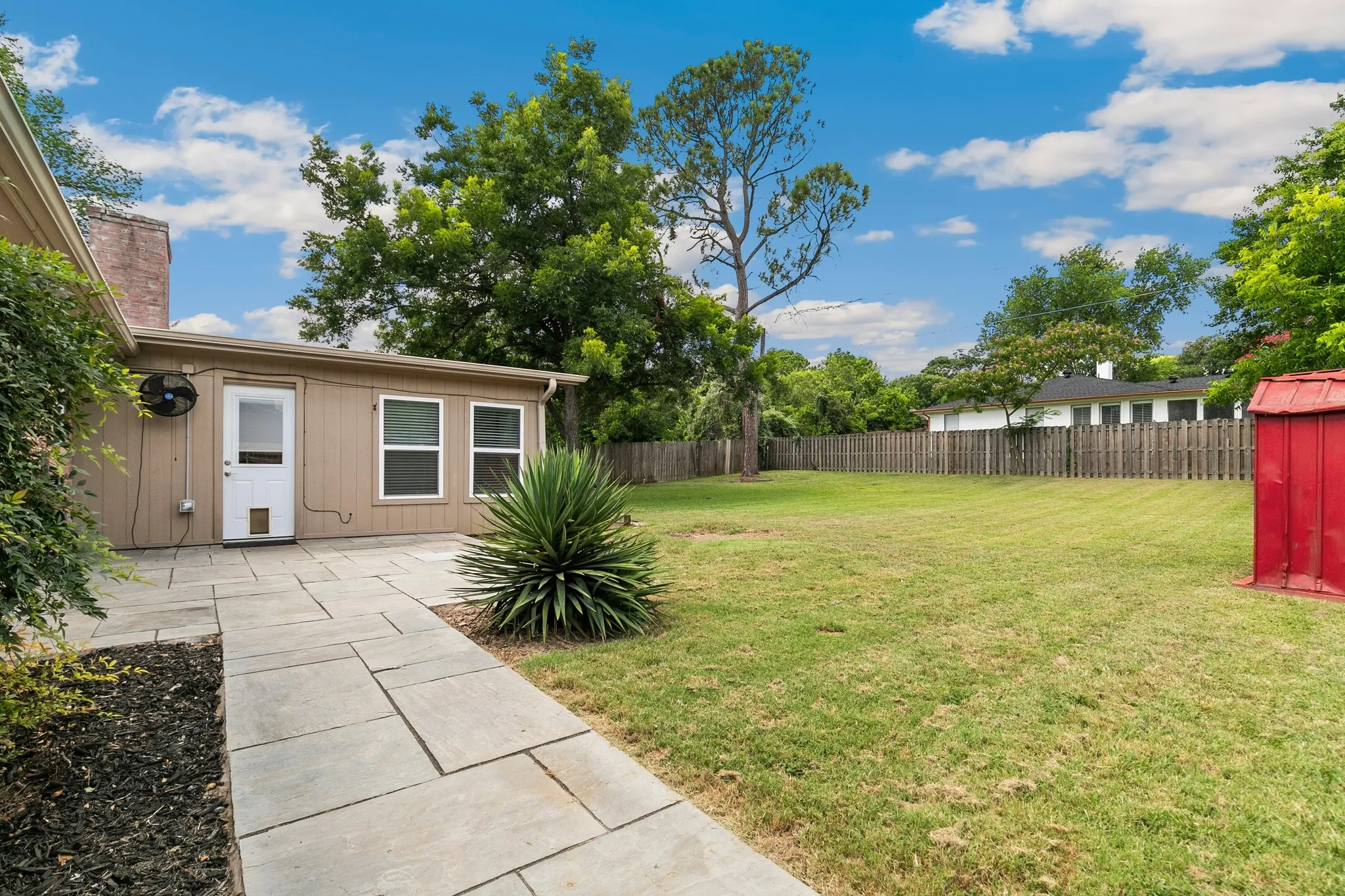 Expansive backyard featuring a large grass area, wood privacy fence, and a stone paver patio