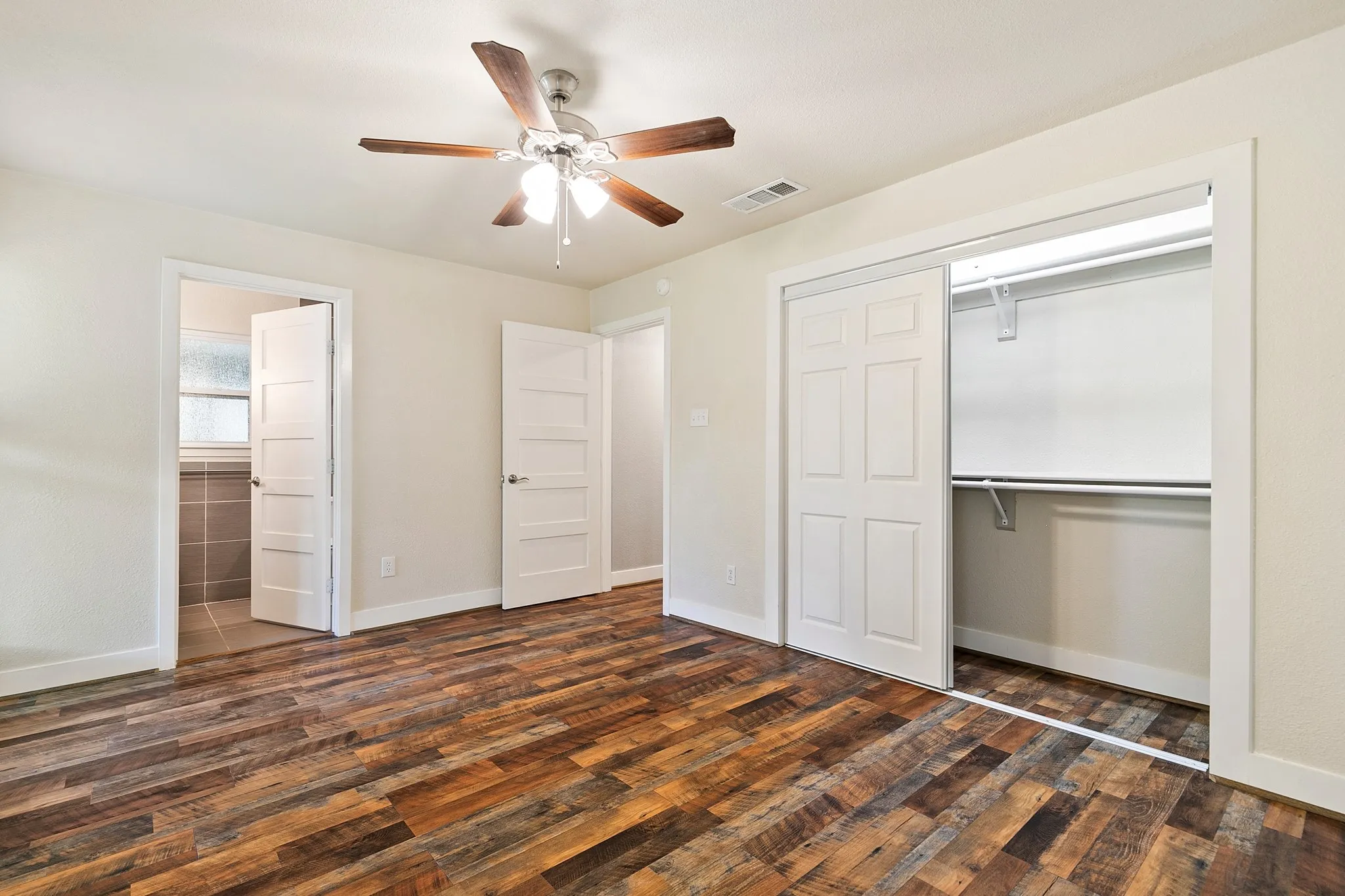 Primary bedroom. Wood-finish flooring throughout, ceiling fan with integrated lighting, white interior doors, and a sliding door closet with shelving and hanging rods