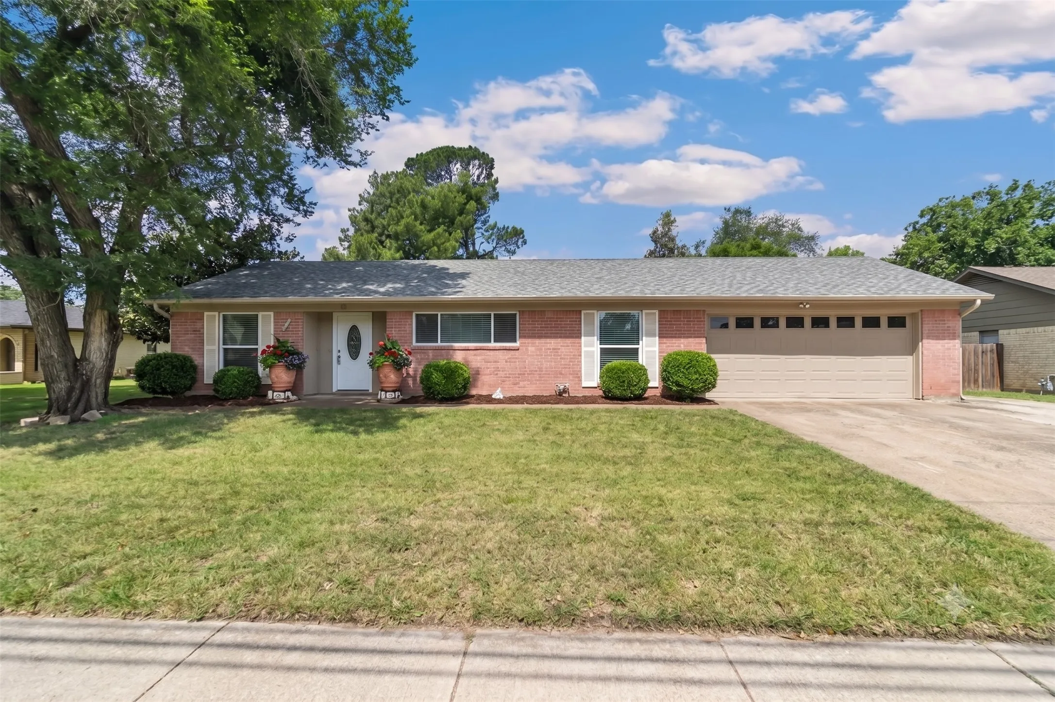 Brick exterior with a gray shingle roof, attached two-car garage, and a concrete driveway
