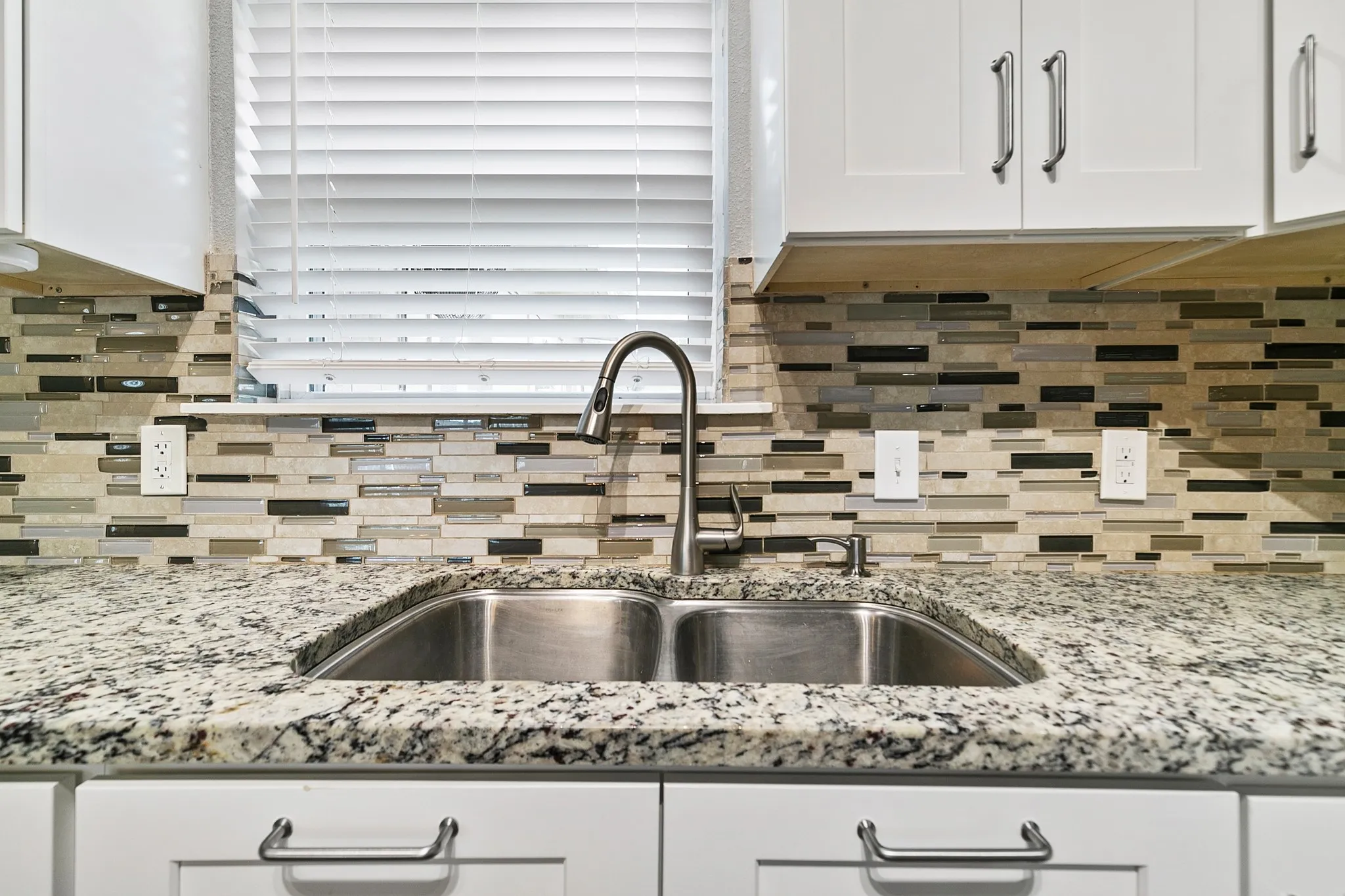 White cabinetry with brushed nickel hardware, speckled countertop, dual basin stainless steel sink with gooseneck faucet, and mosaic tile backsplash
