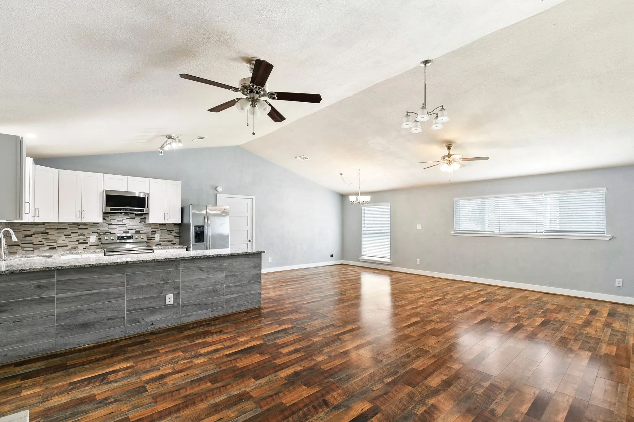 Vaulted ceilings with multiple ceiling fans, wood-finish flooring, white cabinetry, tile backsplash, and a breakfast bar with a stone-finish countertop
