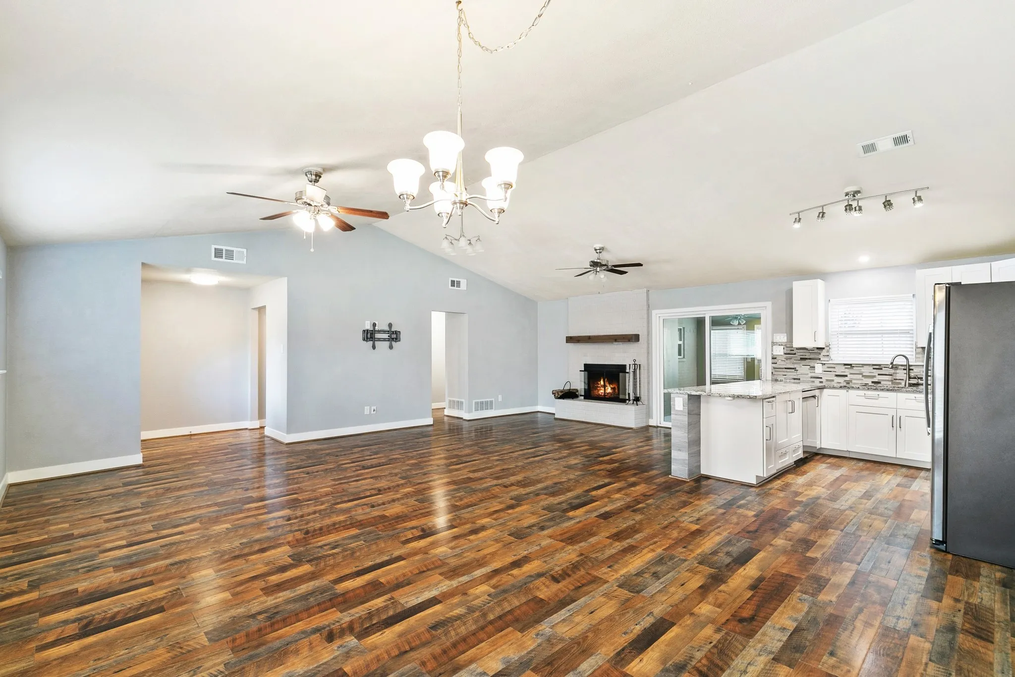 Vaulted ceiling with a chandelier, wood-finish flooring, fireplace, kitchen island, and sliding glass doors