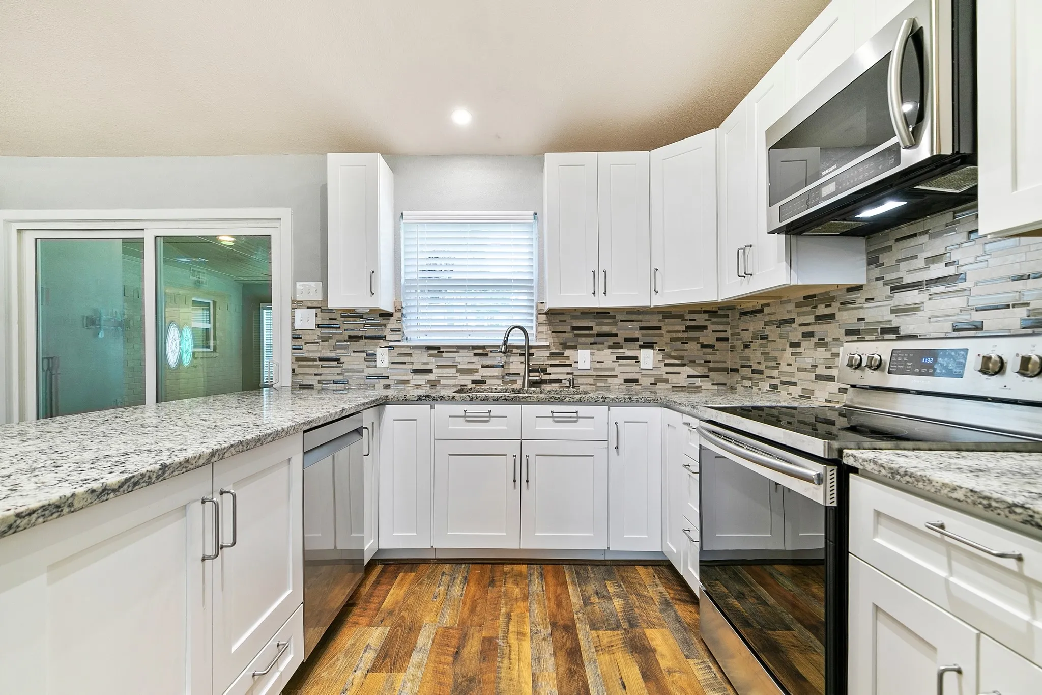 Kitchen featuring white shaker cabinetry, stainless steel appliances, speckled countertops, and a mosaic tile backsplash