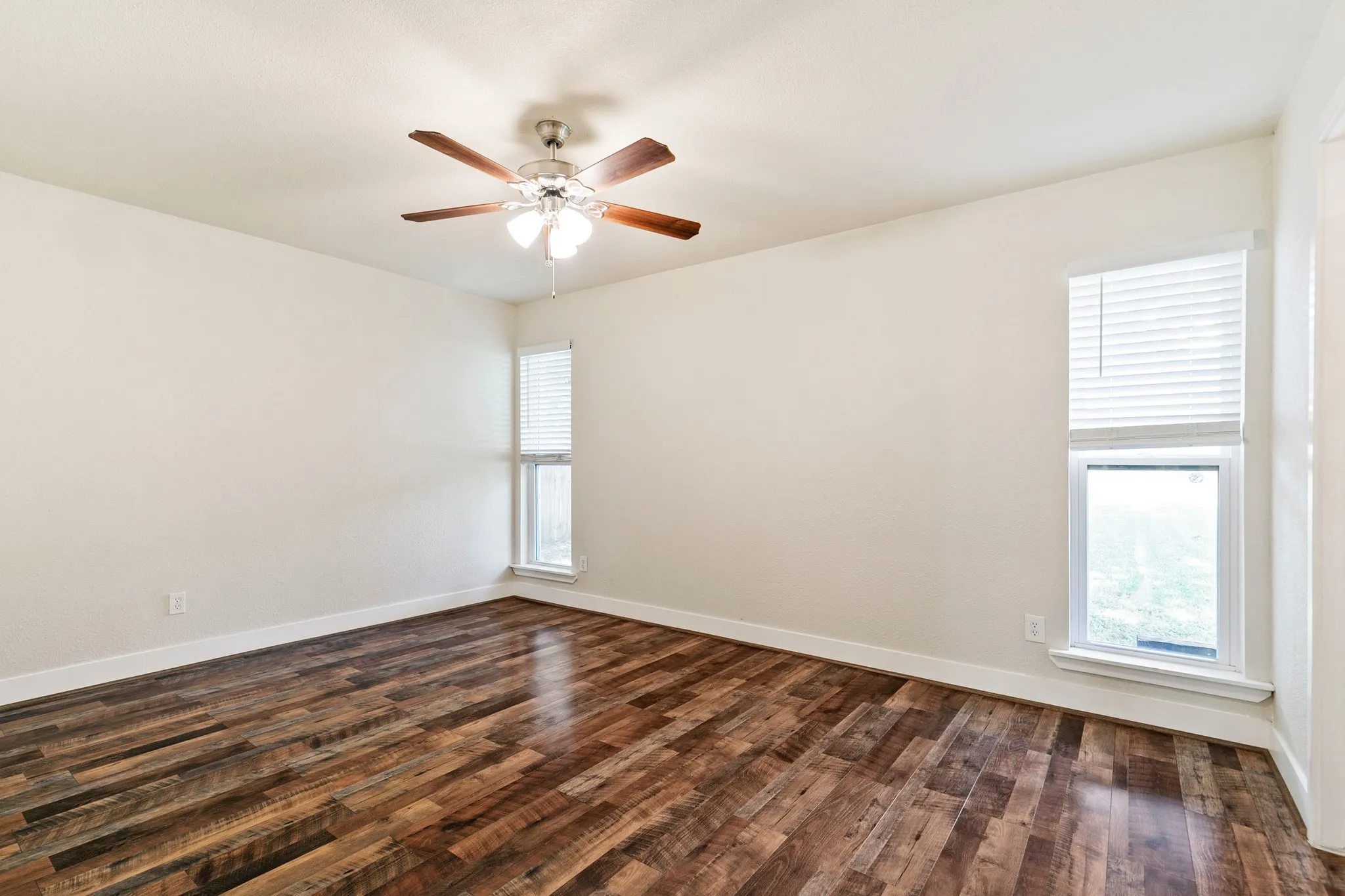 Primary bedroom. Wood-finish flooring, ceiling fan with light fixture, and multiple windows with blinds