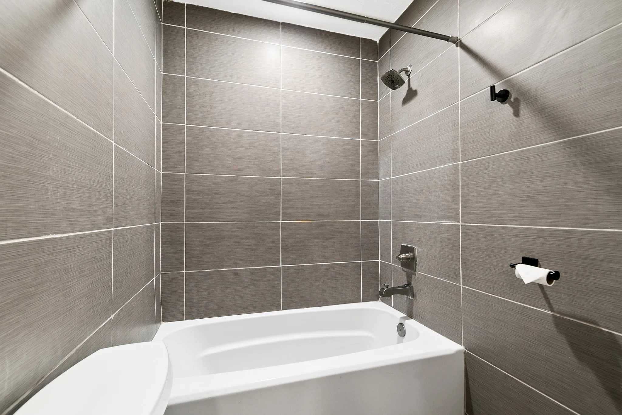 Primary bathroom. Bathtub with a shower fixture, matte black shower rod, and gray tile surround