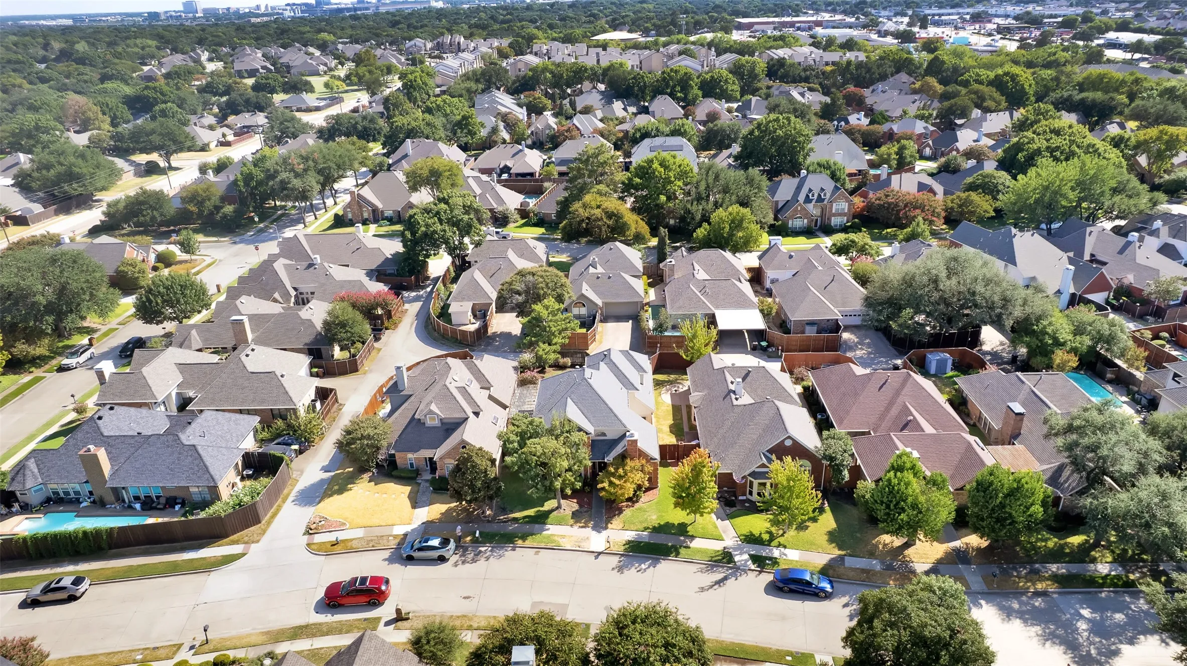 Aerial perspective of a residential neighborhood with mature trees, established homes, and paved streets