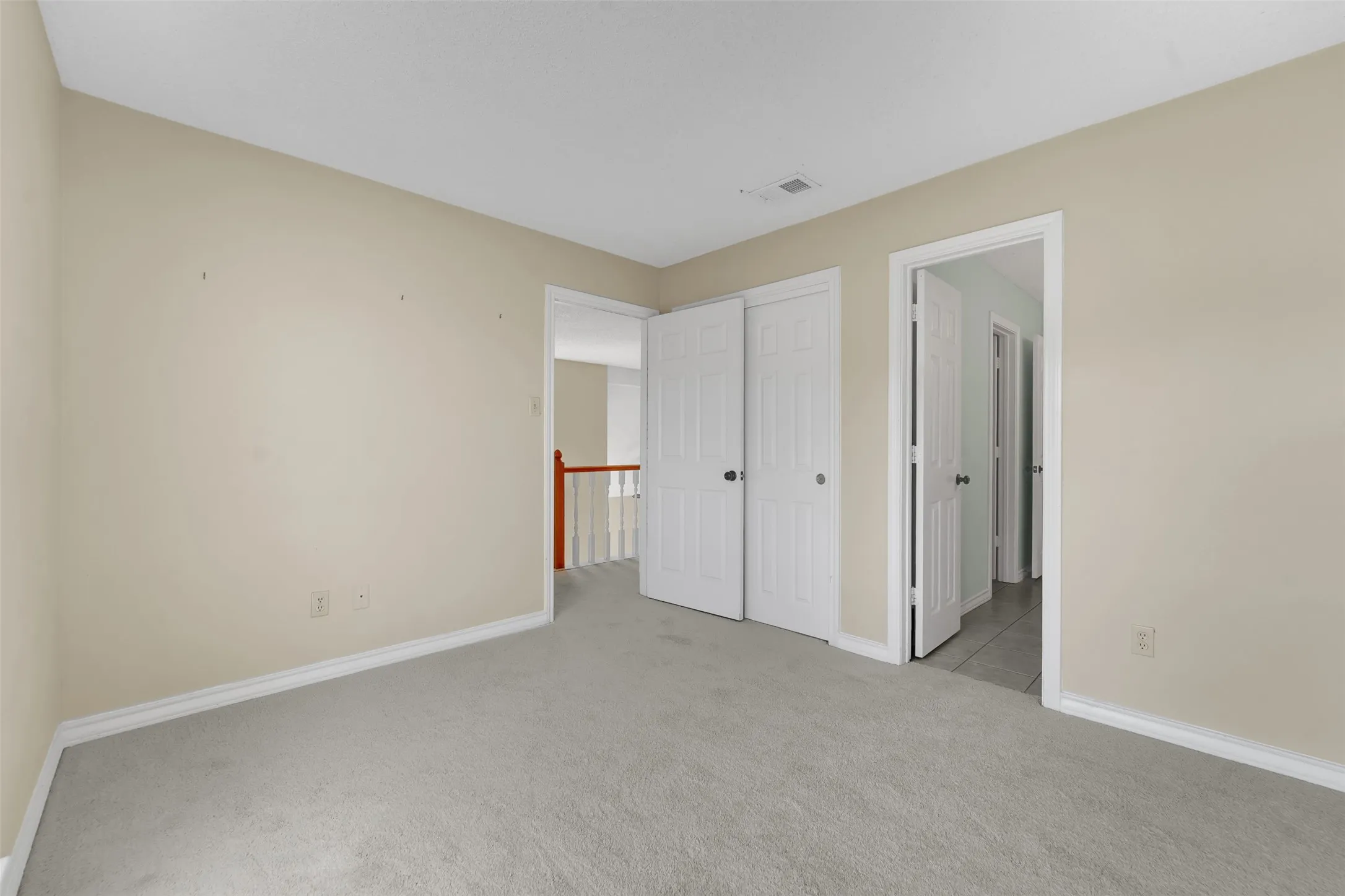 Neutral tone wall paint, light-colored carpeting, white trim, and white bi-fold closet doors