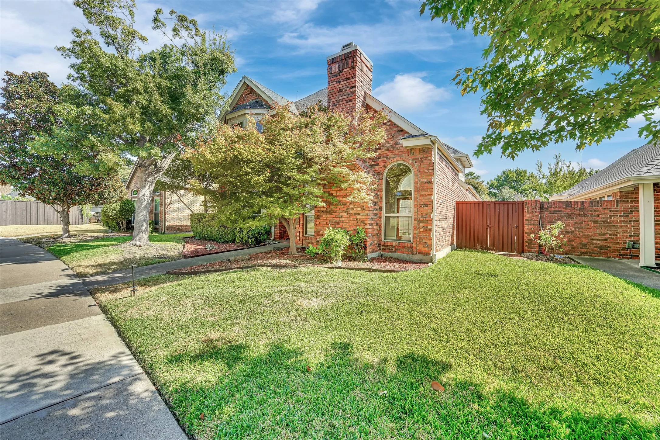 Brick exterior with an arched window, a prominent chimney, and mature landscaping