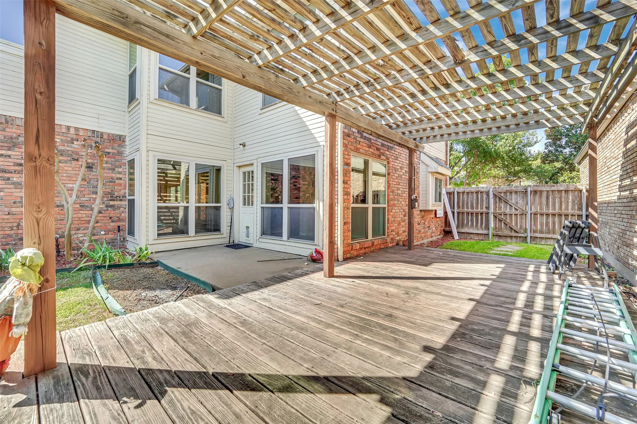 Expansive wood deck with an overhead pergola, complemented by a concrete patio, brick exterior, and a wood privacy fence