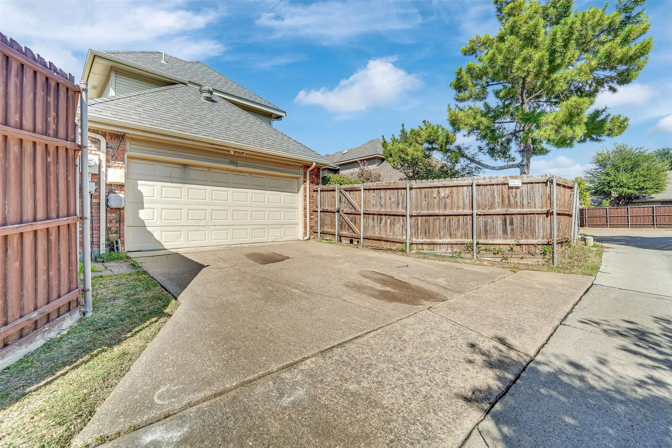 Attached two-car garage with a concrete driveway, complemented by a wood fence and mature trees
