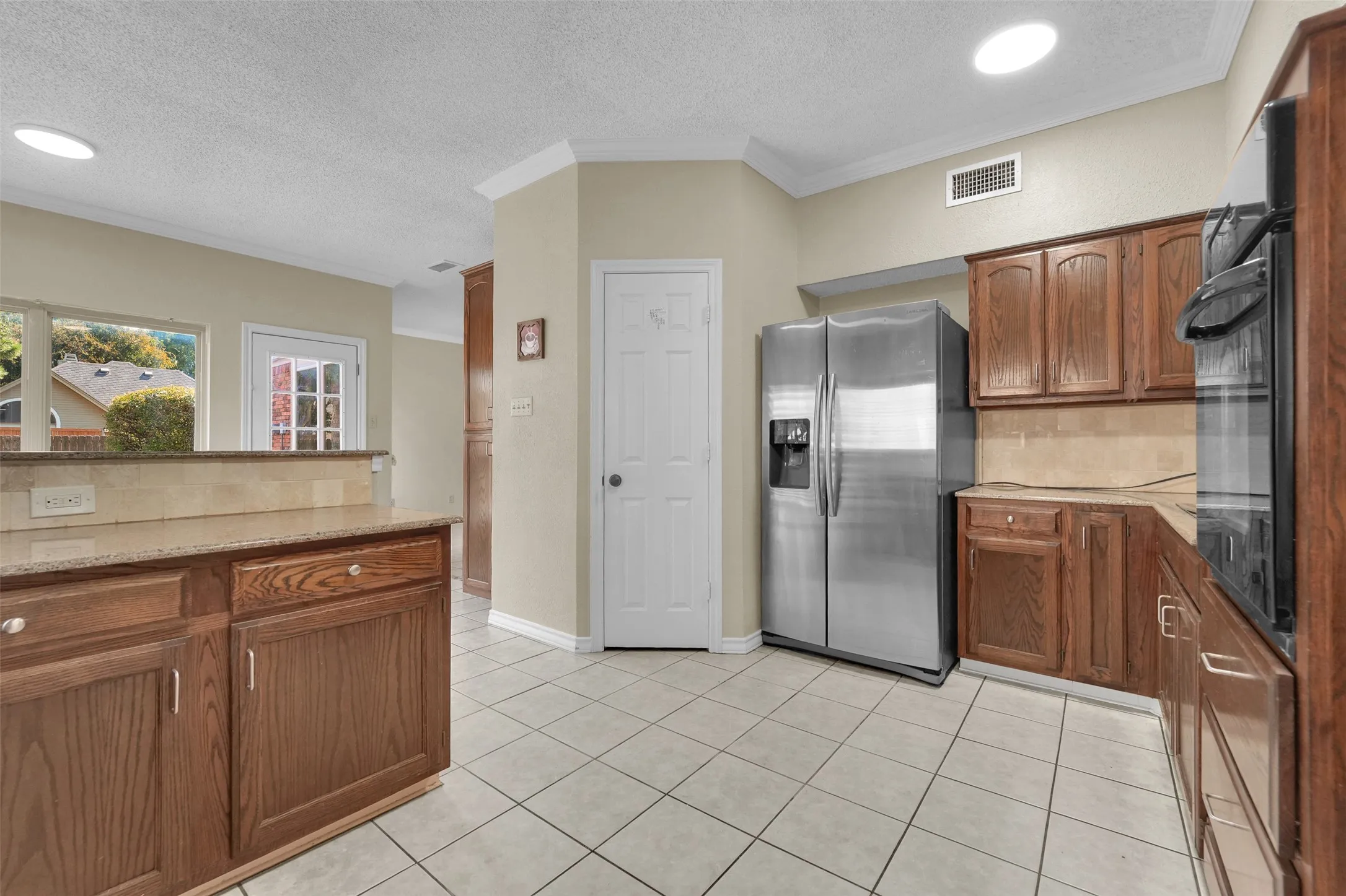 Kitchen with tile flooring, wood-finish cabinetry, stainless steel refrigerator, and recessed lighting
