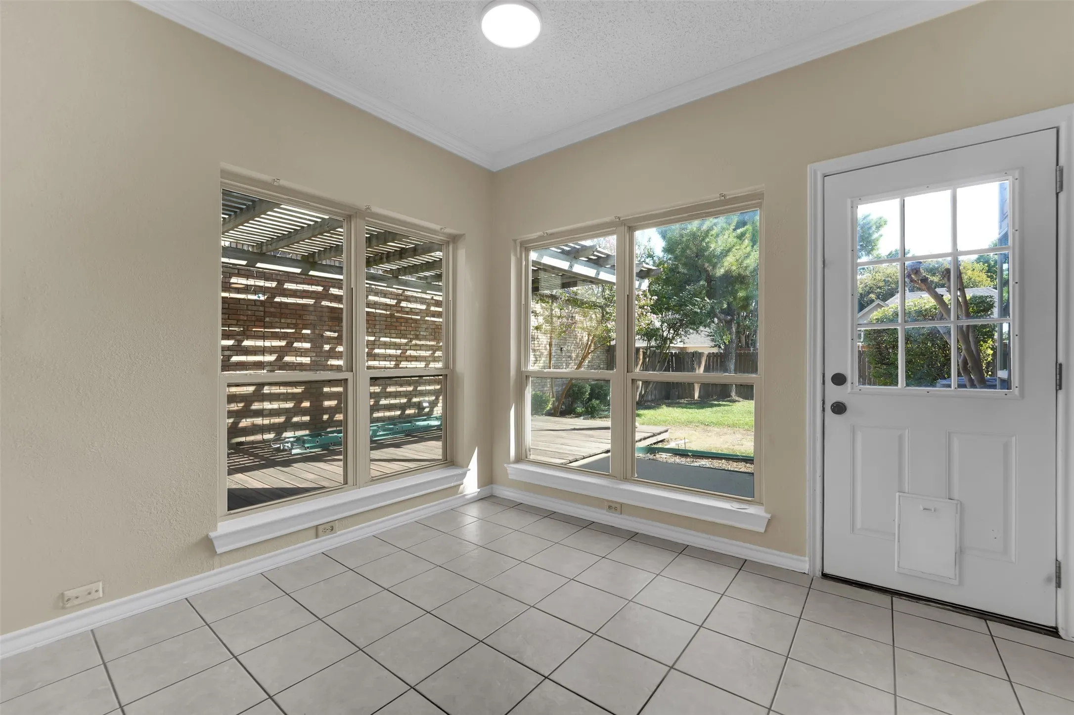 White tile flooring, multiple large windows, recessed lighting, and a white paneled door with glass inserts