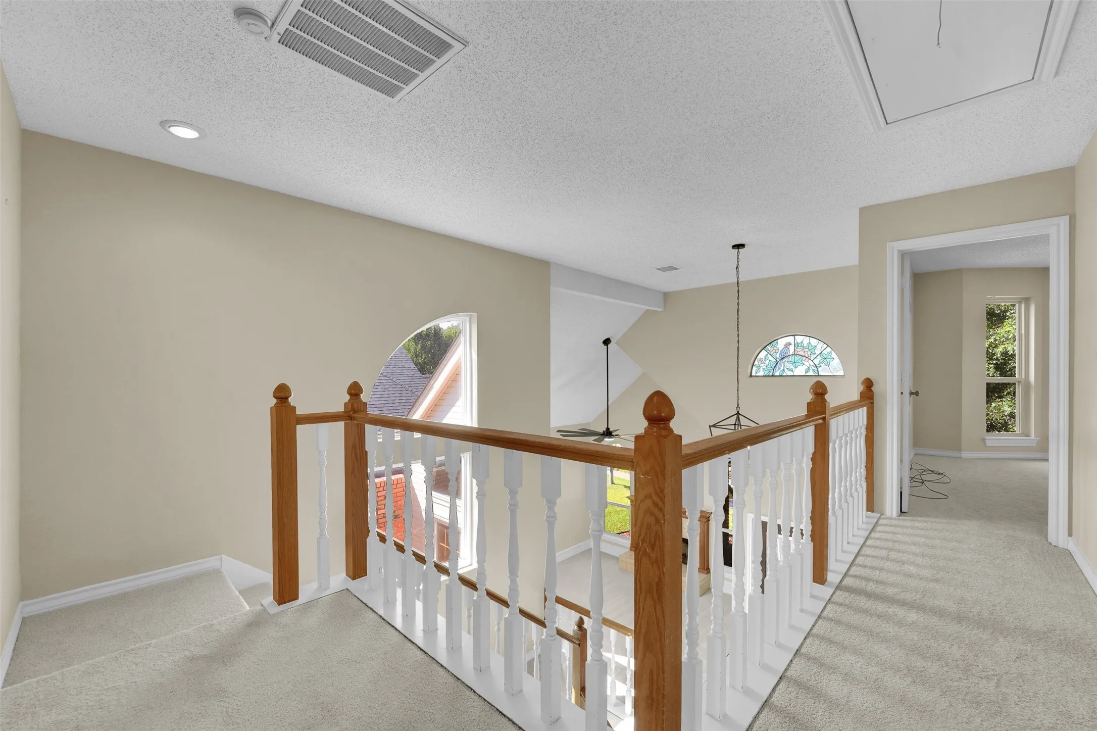 Carpeted upper landing with wooden handrail, white balusters, recessed lighting, and a decorative stained glass arched window