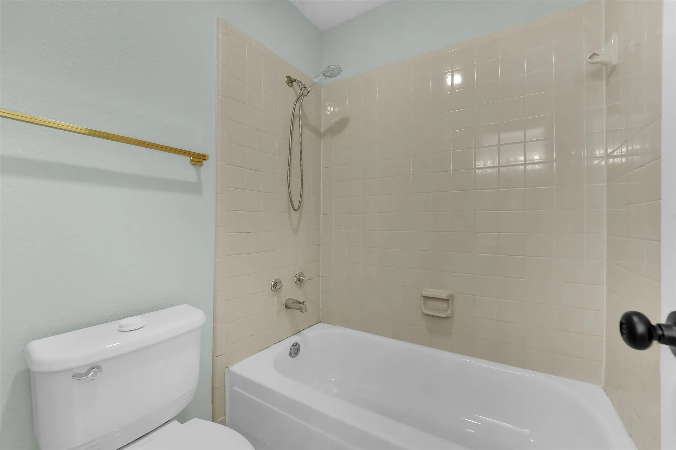 White porcelain bathtub with a shower head and tile surround
