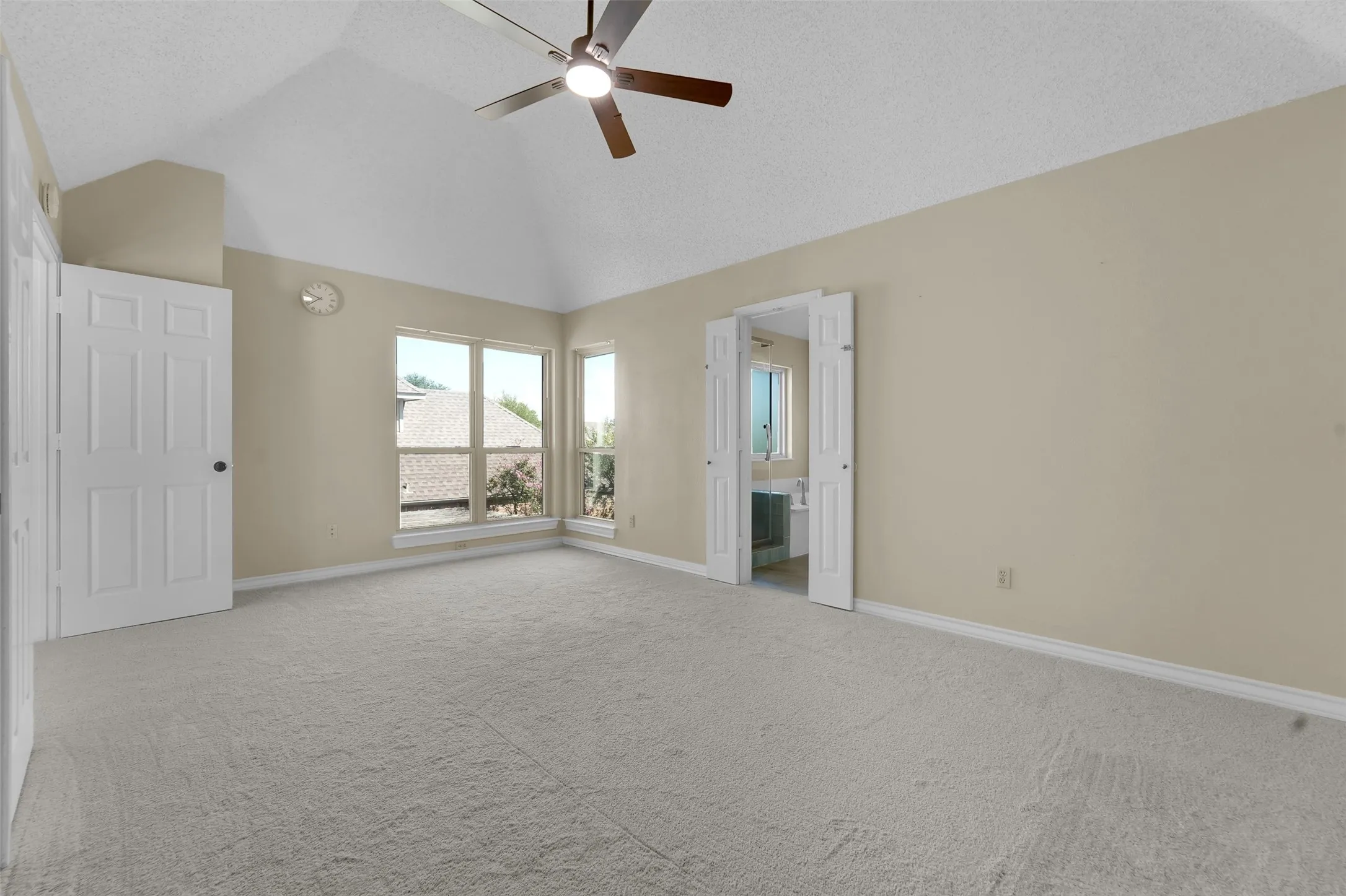 Vaulted ceiling with a ceiling fan, light-toned carpeting, ample natural light, and a bi-fold door entryway
