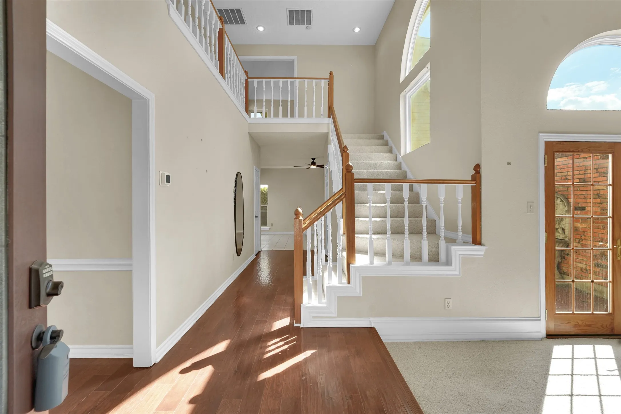 Two-story foyer featuring wood-finish flooring, a grand staircase with wood railings, a multi-pane glass entry door, and arched transom windows