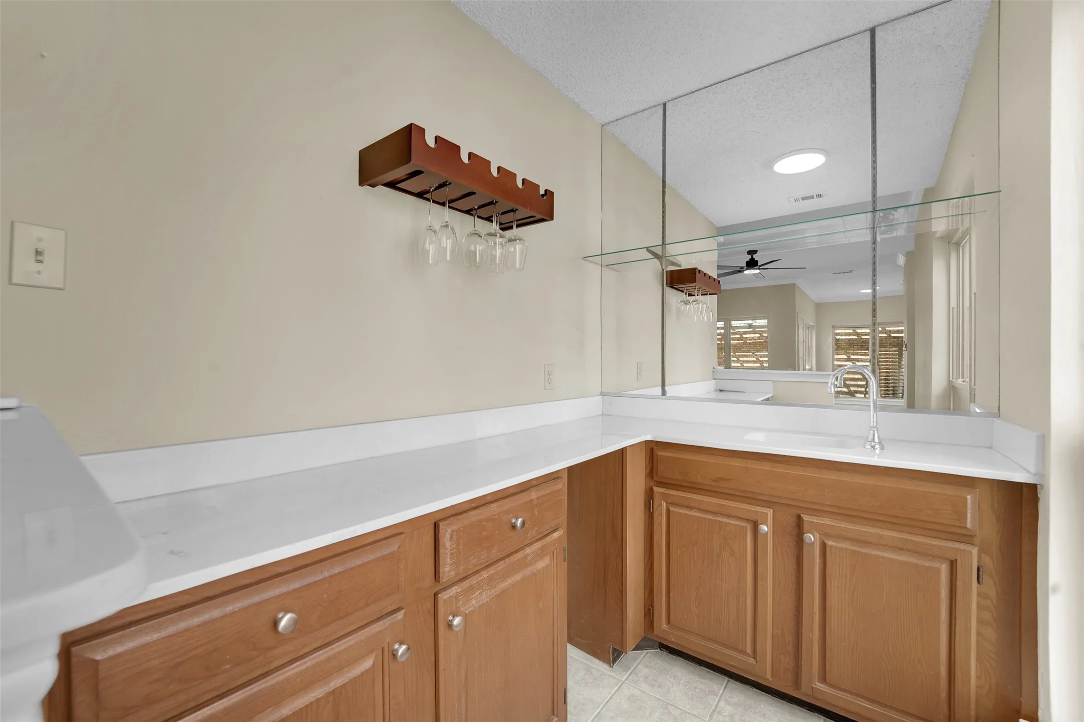 Built-in wet bar featuring wood cabinetry, white countertops, an integrated sink with a faucet, and an overhead mirror with a glass shelf