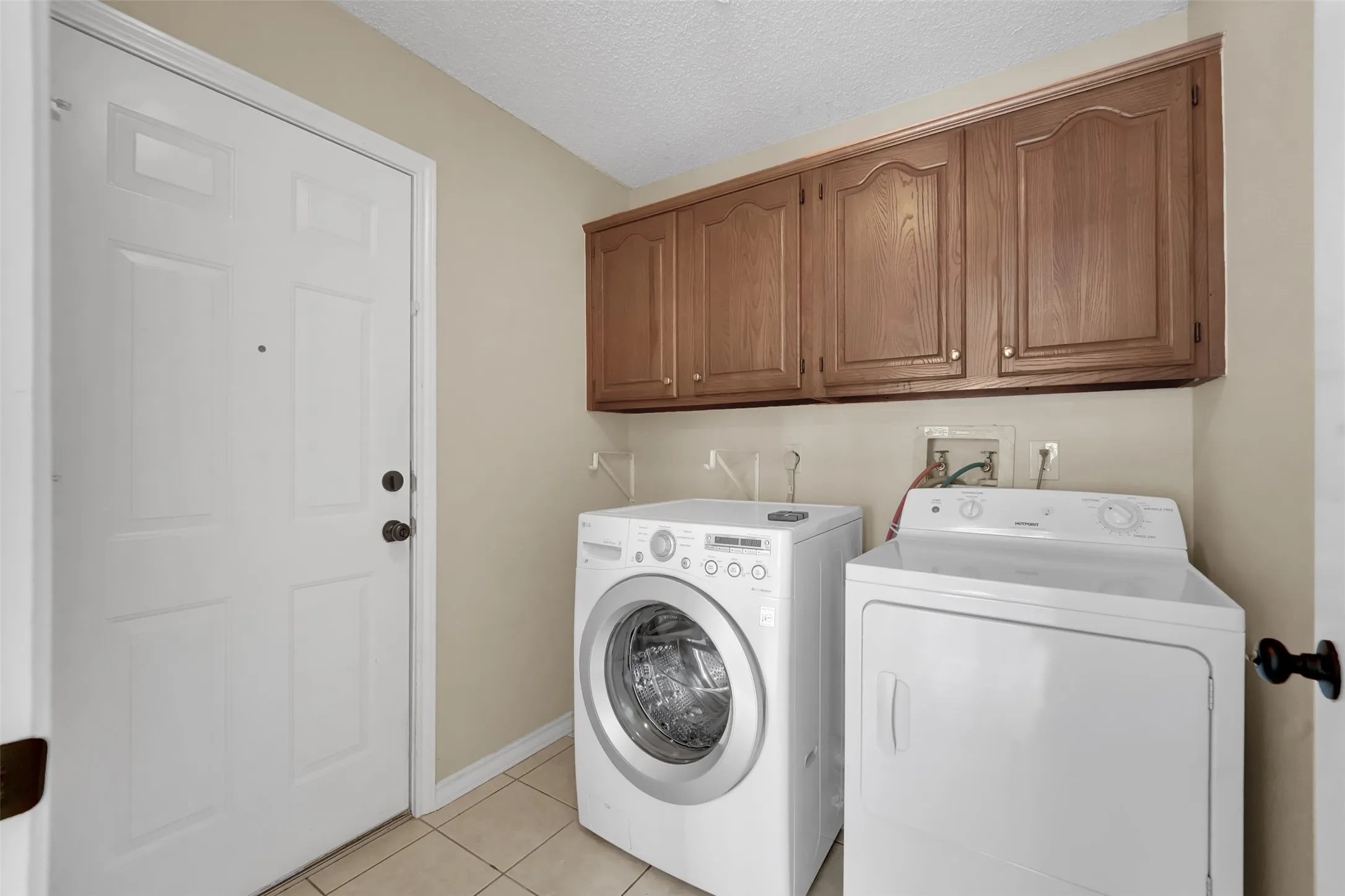 Laundry area with upper wood cabinetry and tile flooring