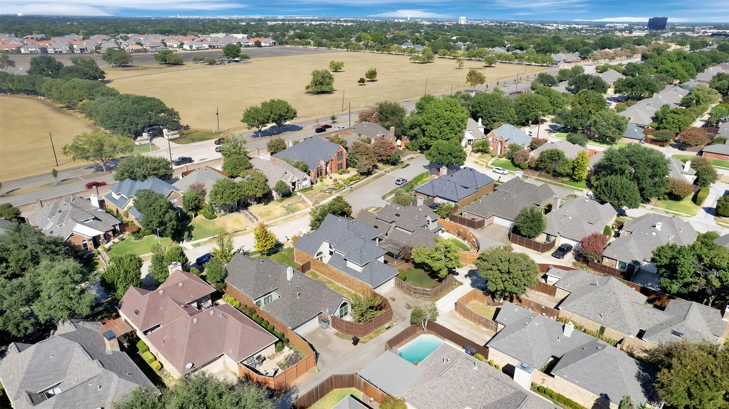 Aerial perspective showcasing a residential area with mature trees, varied rooflines, and a nearby open field