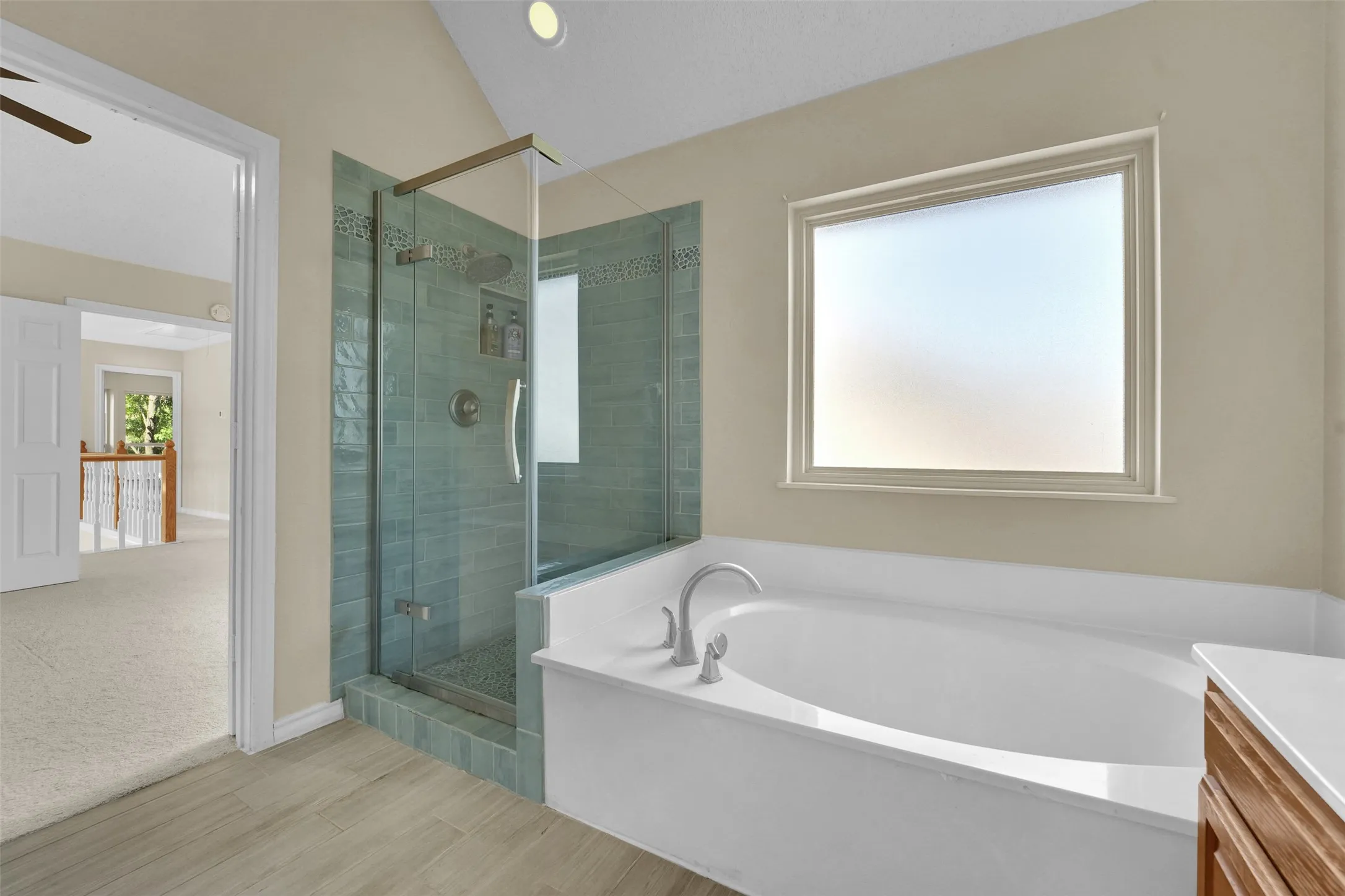 Soaking tub with brushed nickel fixtures, a glass-enclosed shower with blue-toned tile, and wood-finish flooring