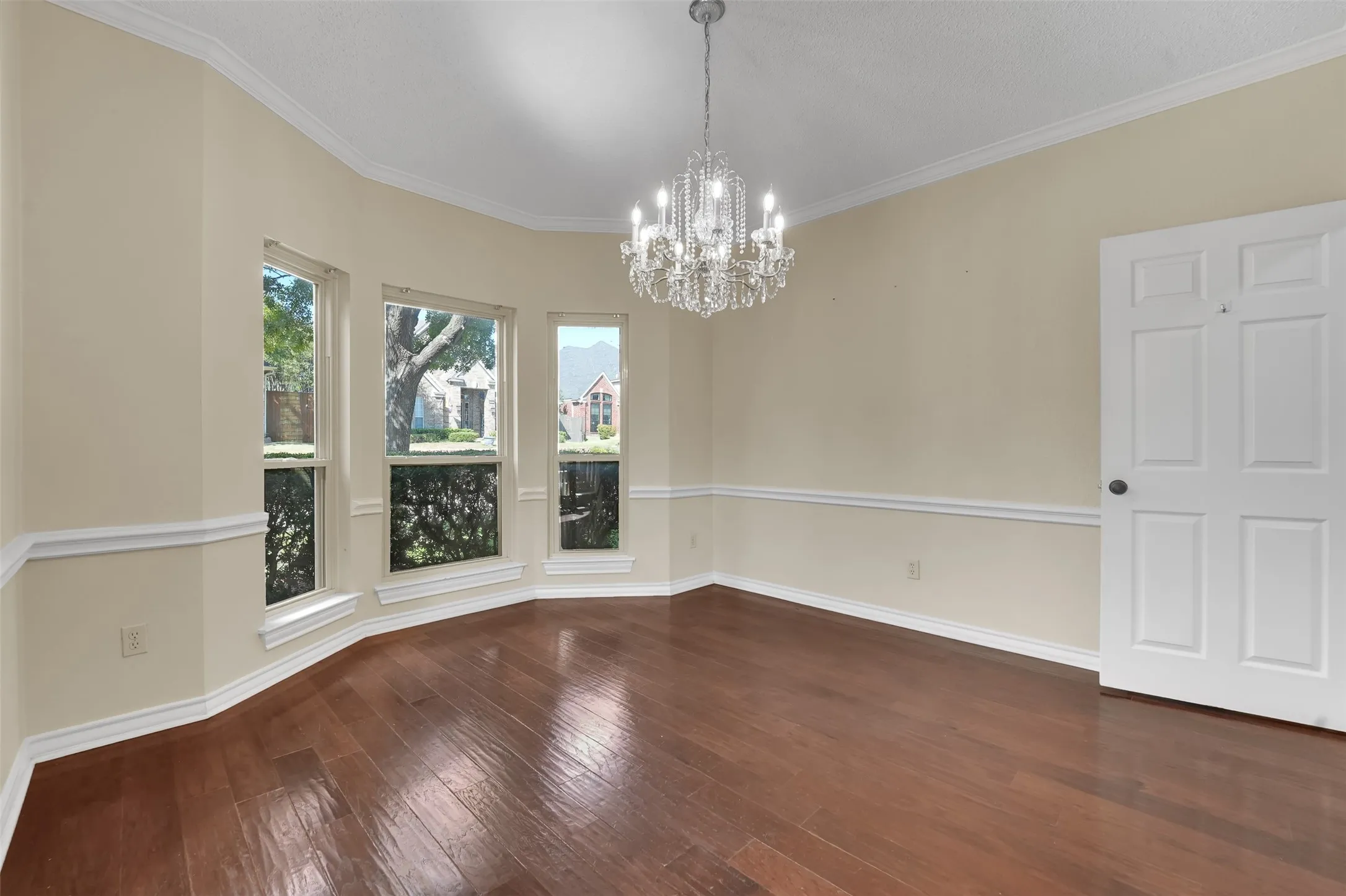 Hardwood flooring, bay window configuration, crown molding, chair rail molding, and a crystal chandelier