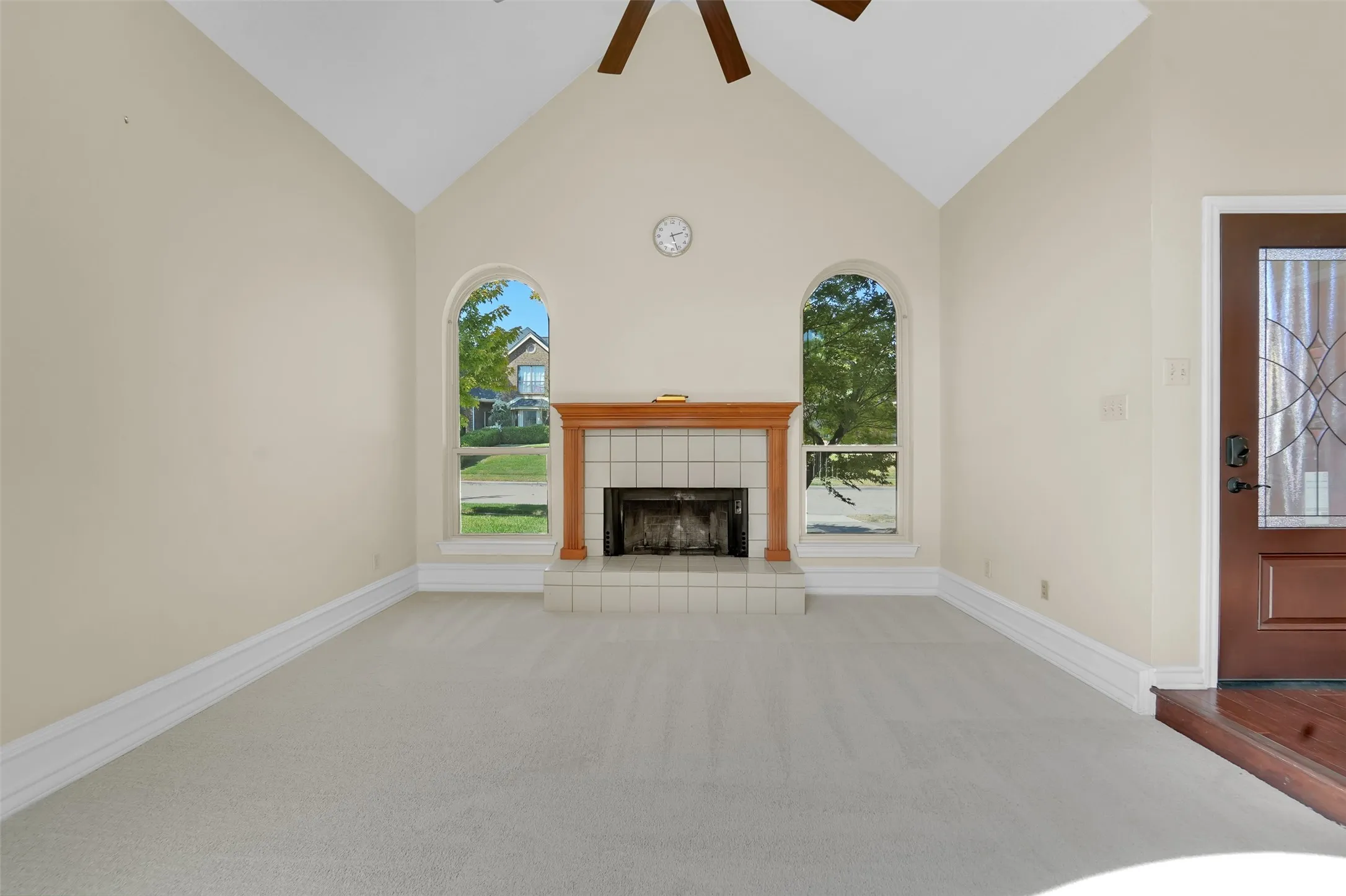 Vaulted ceiling with an exposed beam, two arched windows, tiled fireplace with a wood-finish mantel, and a dark wood-finish entry door with decorative glass