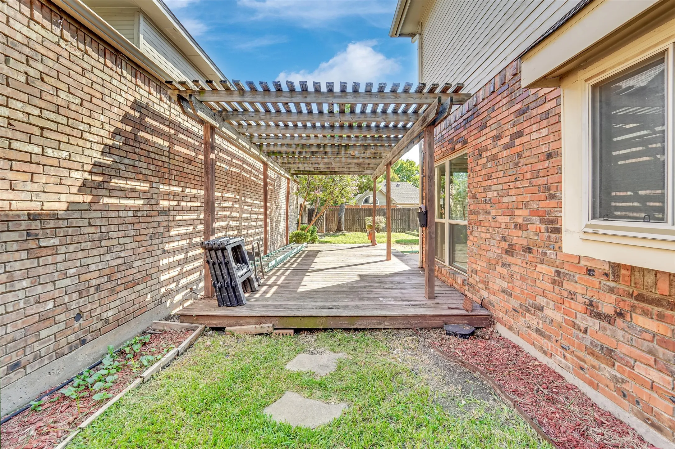 Wood pergola covering a wood deck with brick exterior walls and a grassy area