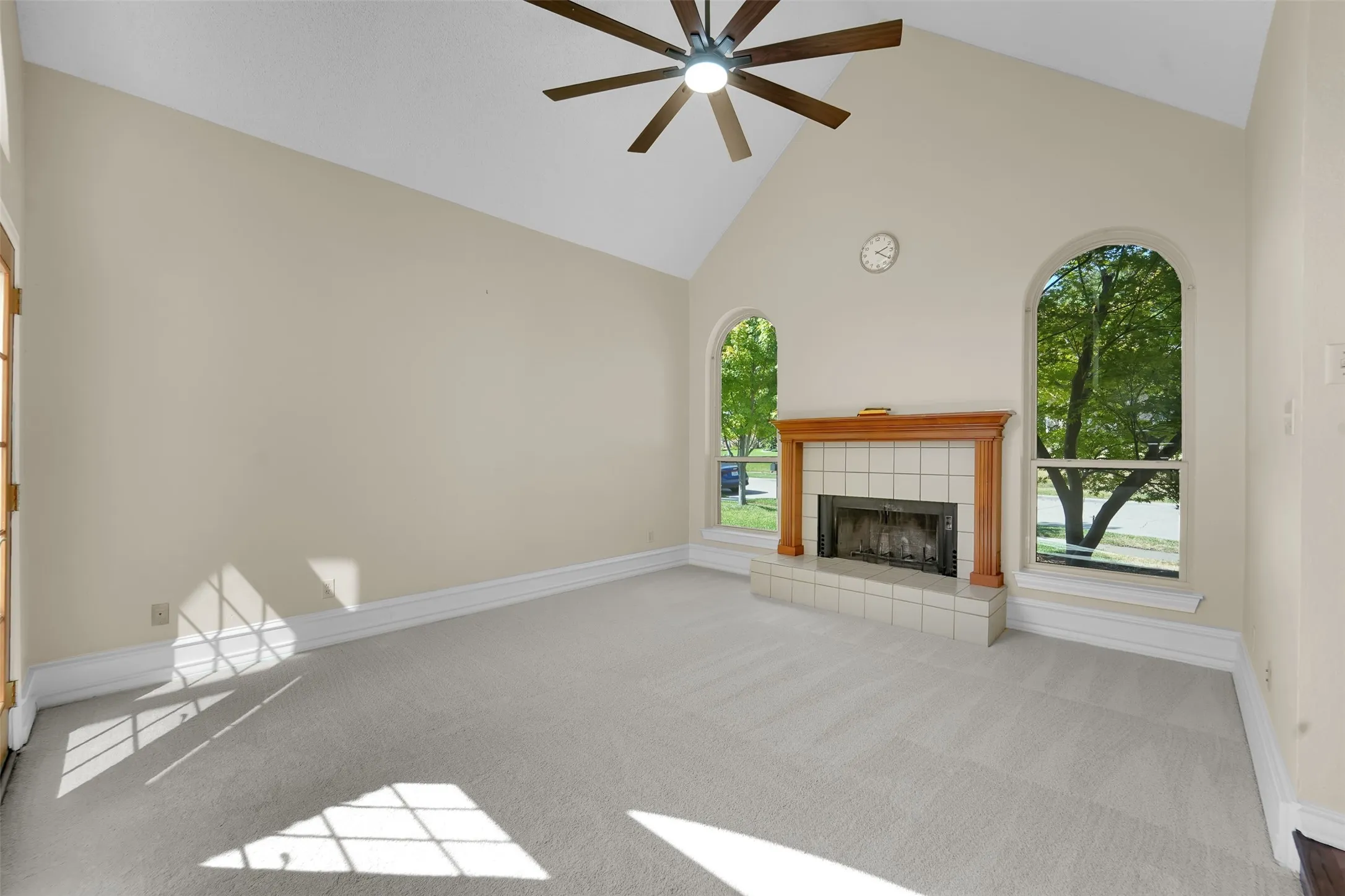 Vaulted ceiling, ceiling fan, wood-mantled fireplace, tiled hearth, and arched windows