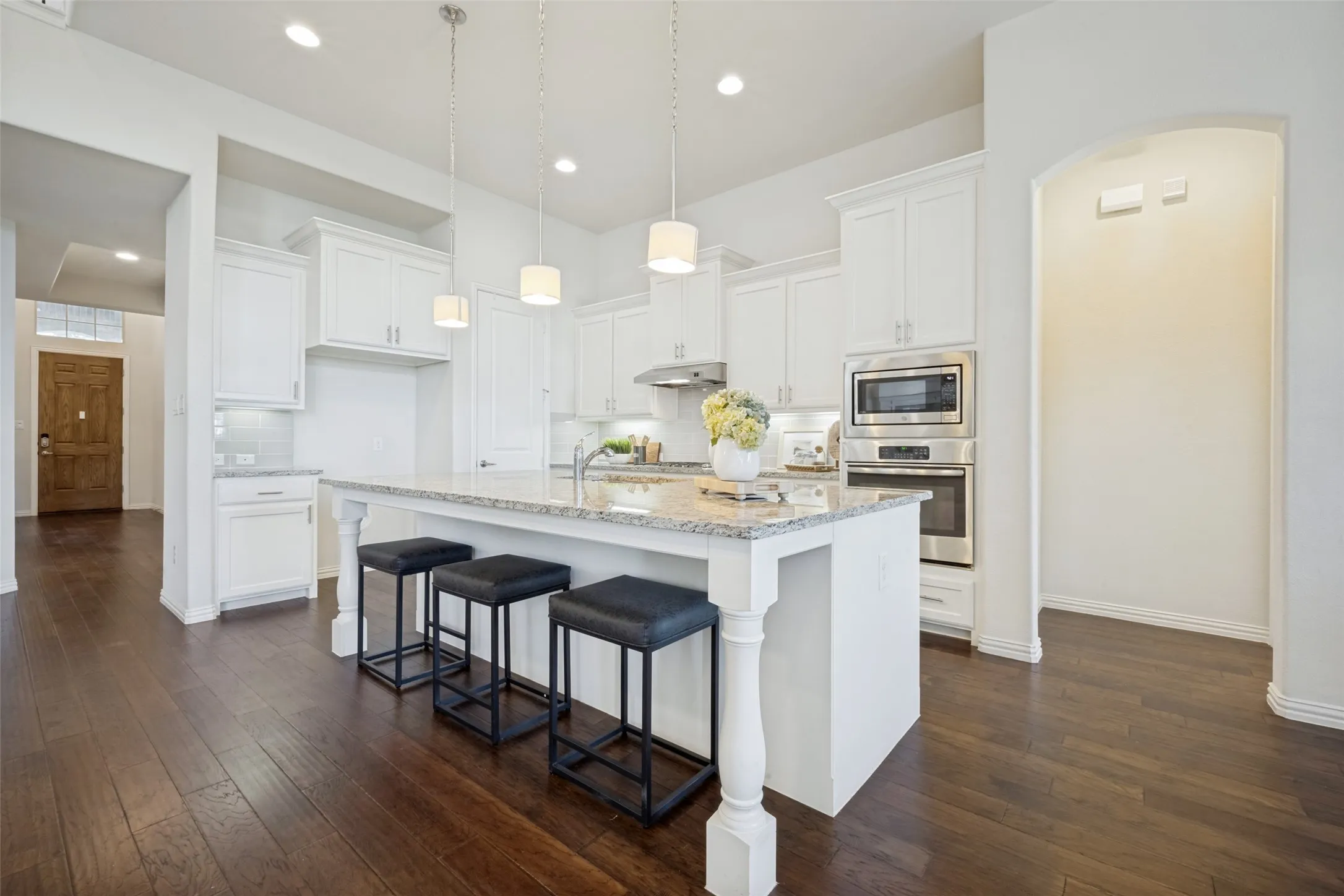 Kitchen featuring white cabinetry, stainless steel appliances, a center island with a granite countertop, pendant lighting, and wood-finish flooring