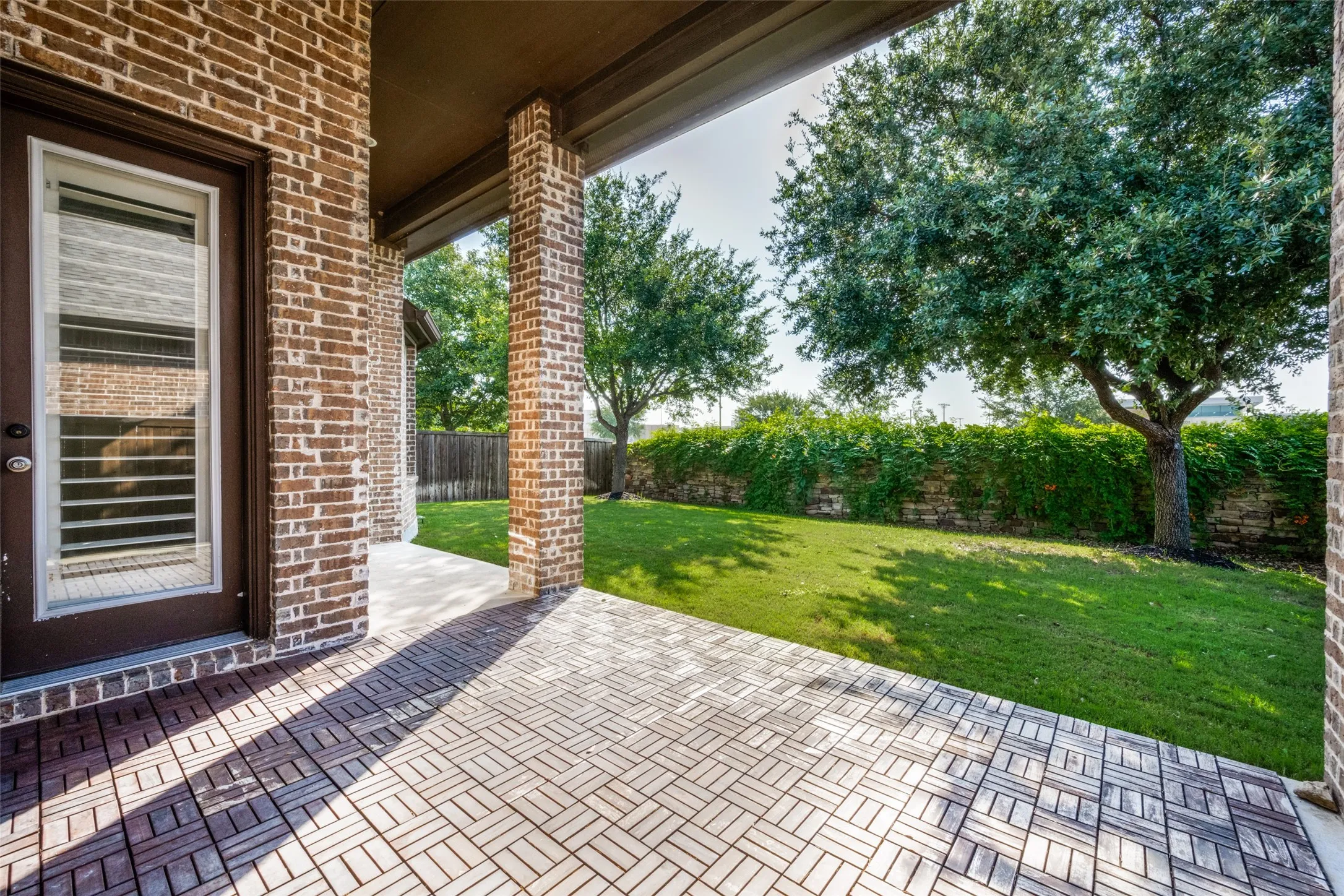 Covered patio featuring a herringbone-patterned paver floor and brick columns