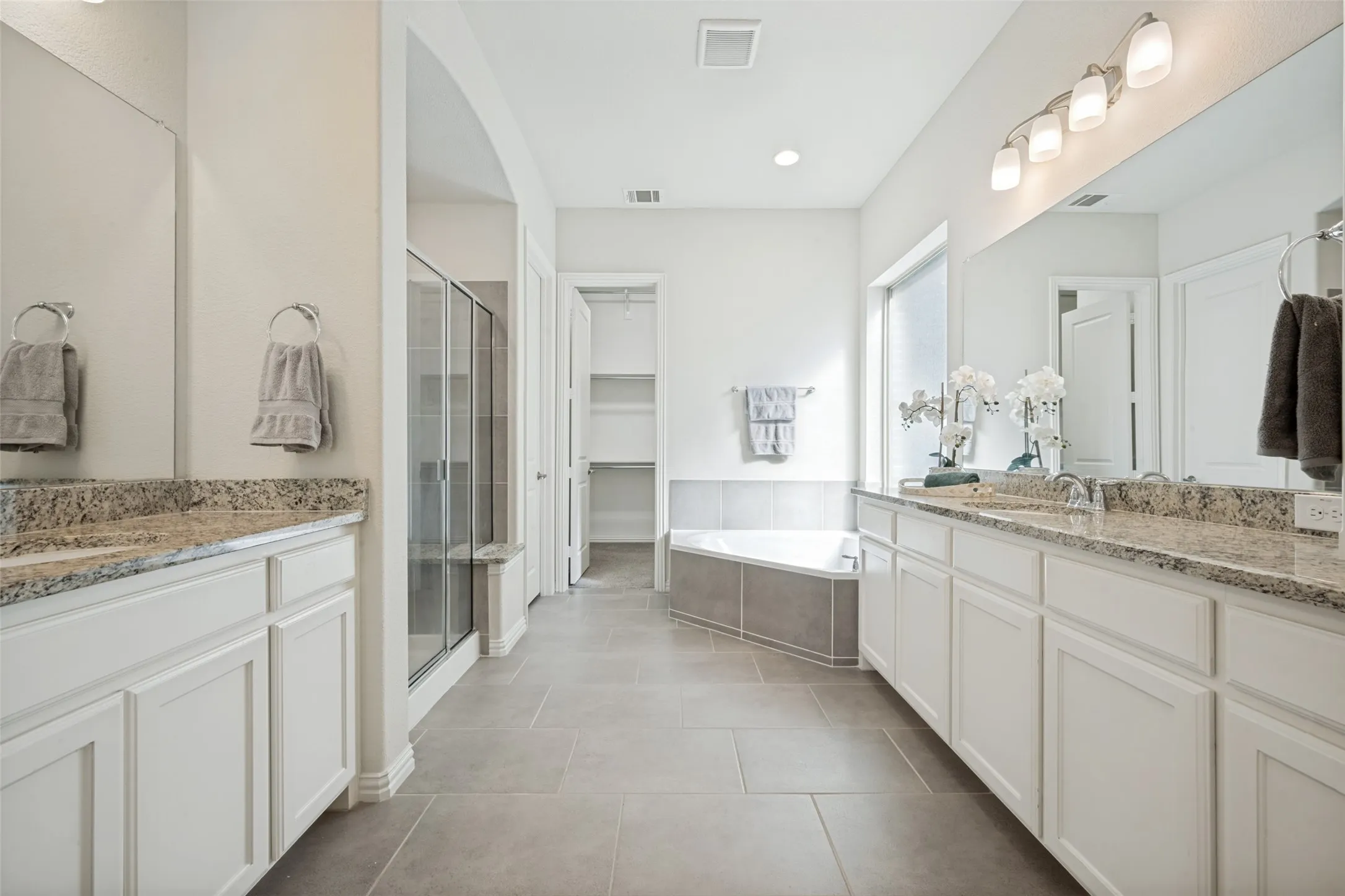 Dual vanity with light-colored countertops, walk-in shower with glass enclosure, separate soaking tub, and tile flooring