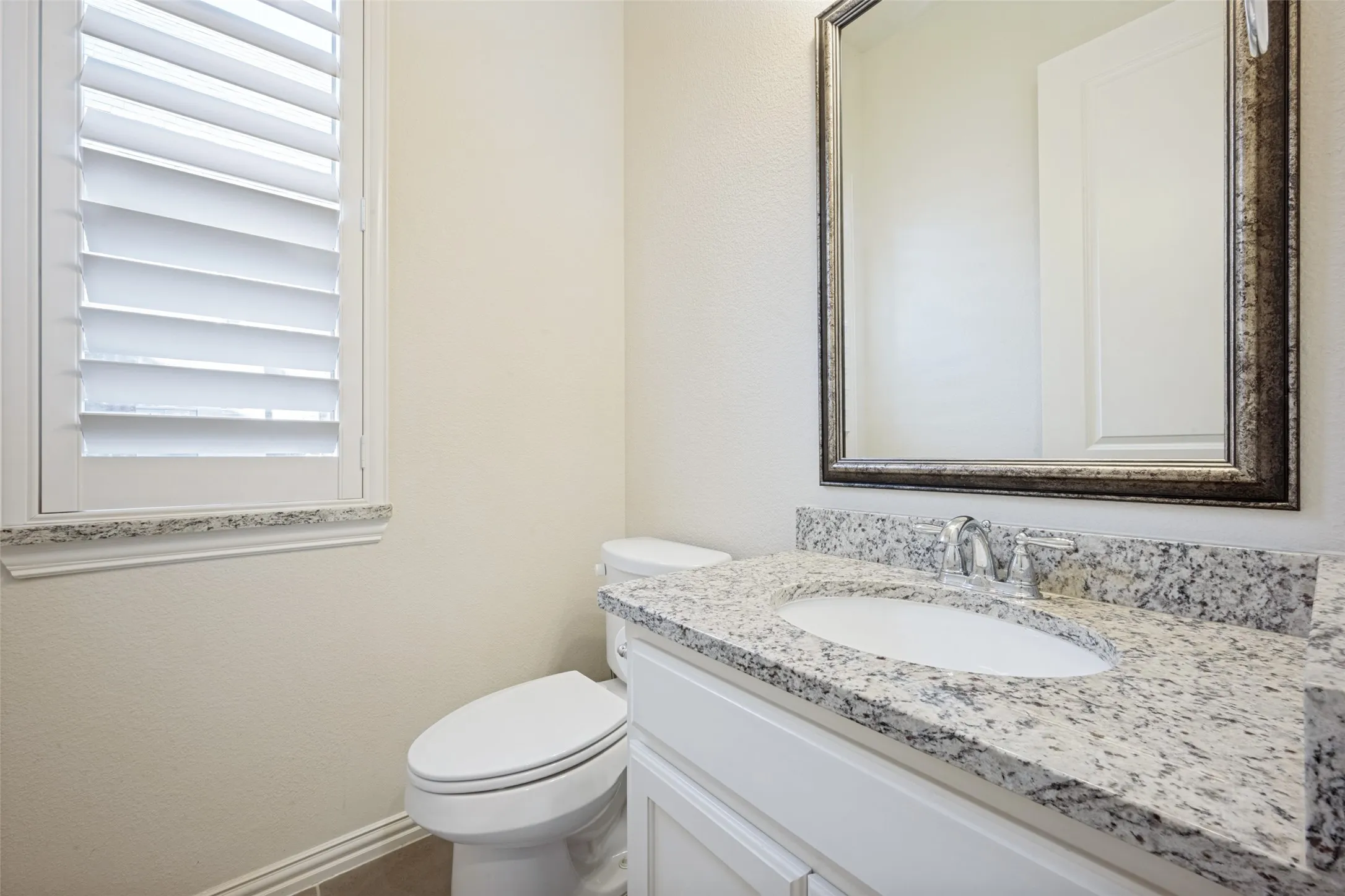 White vanity with an integrated sink, granite countertop, and a framed mirror
