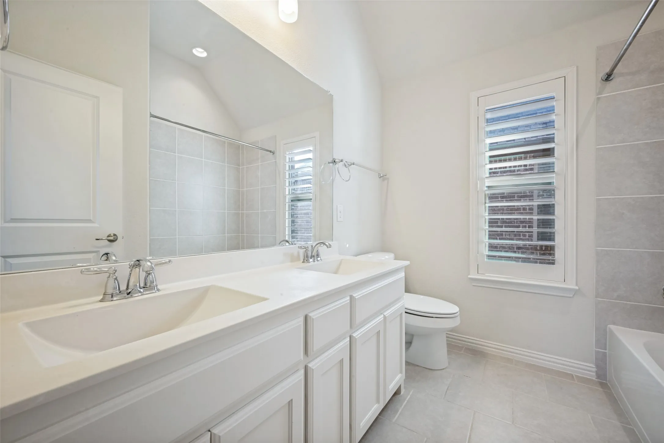 Dual vanity with integrated sinks, white cabinetry, chrome fixtures, tiled flooring, and a window with plantation shutters