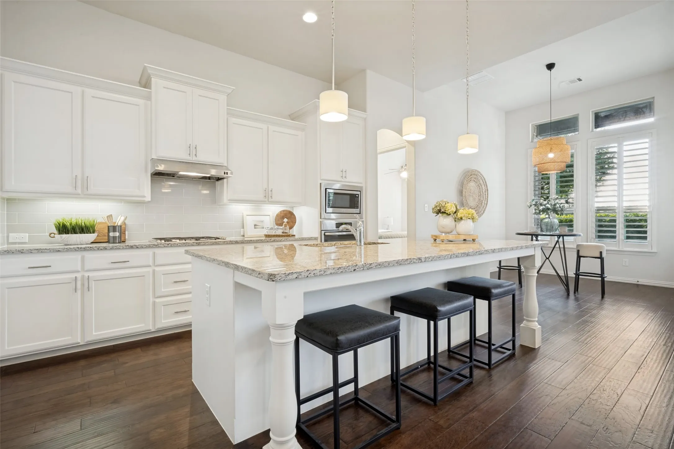 Spacious kitchen featuring white cabinetry, a large island with granite countertops, stainless steel appliances, and wood-finish flooring