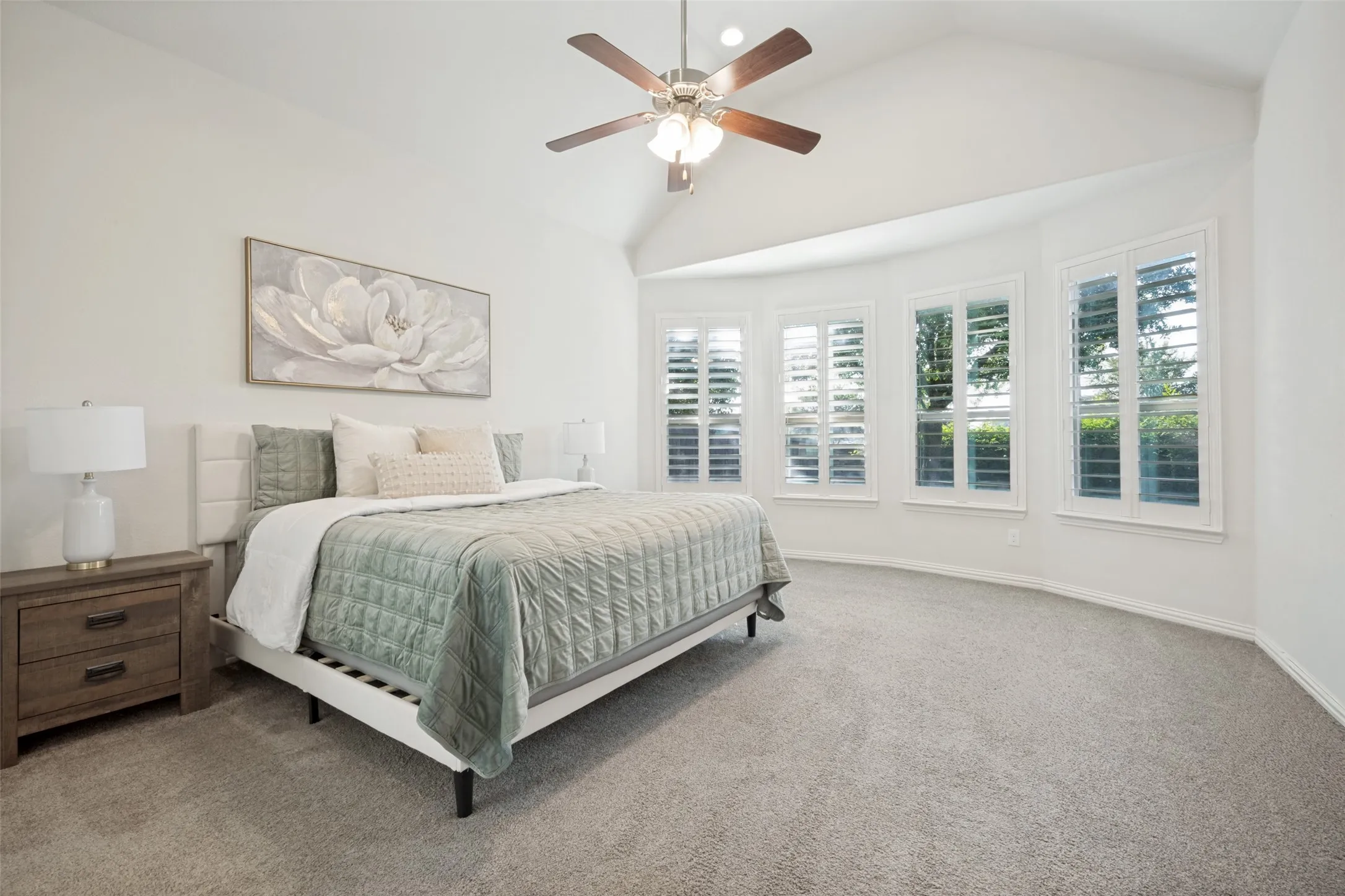 Vaulted ceiling with a ceiling fan, carpeted flooring, and a bay window featuring plantation shutters