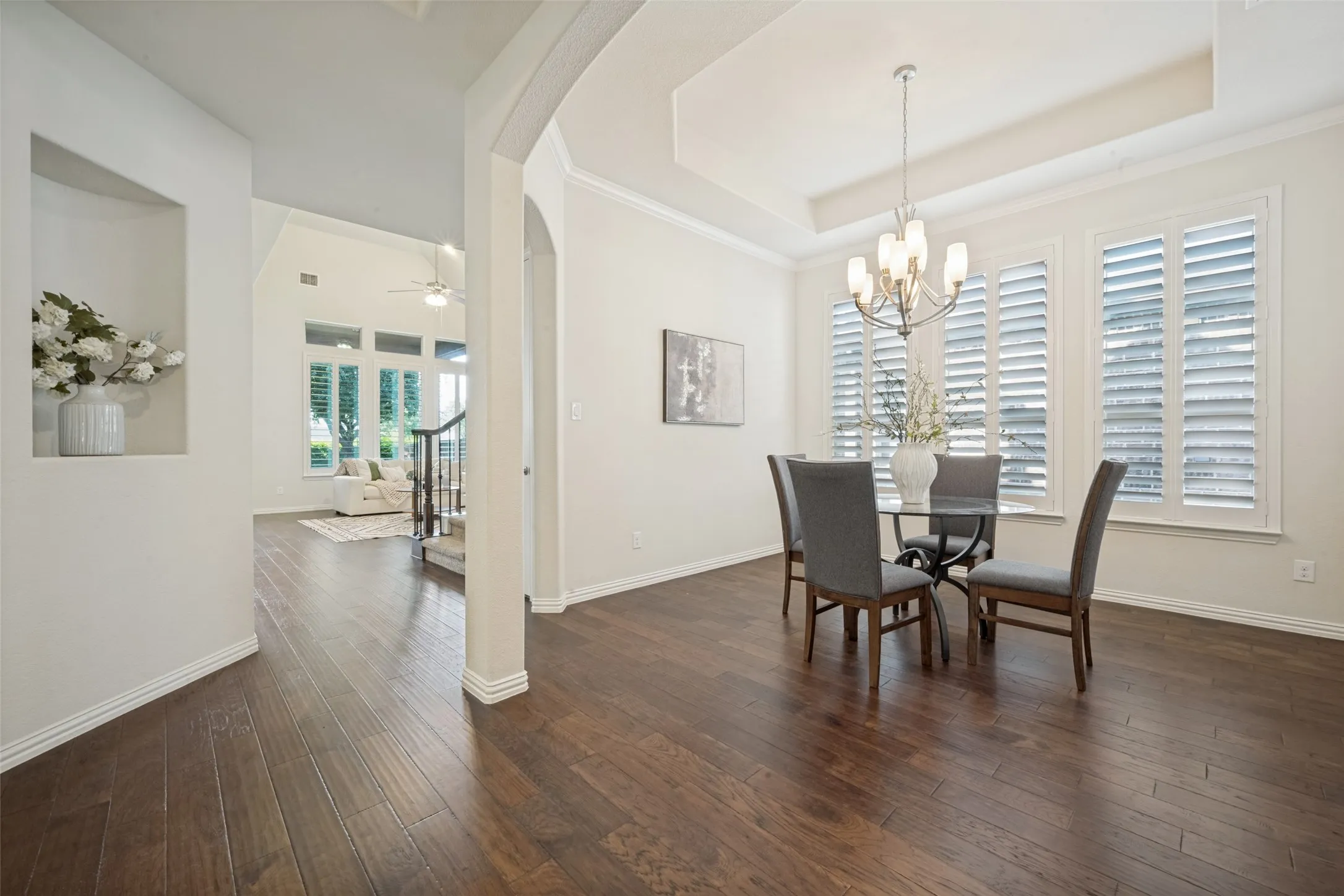 Hardwood-finish flooring throughout, tray ceiling with chandelier, arched entryway, plantation shutters, and recessed wall niche