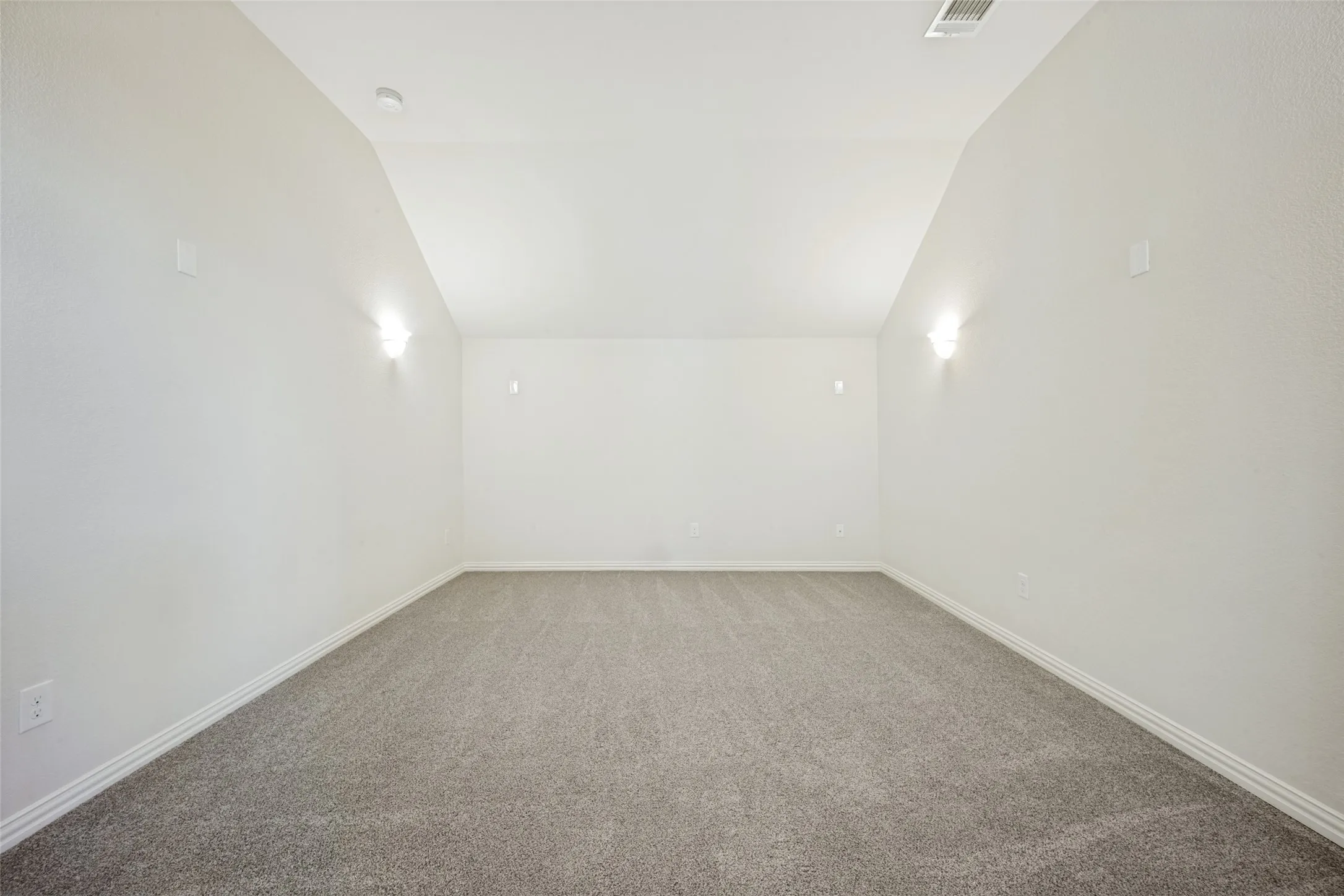 Neutral carpet flooring, sloped ceiling, and wall-mounted sconces