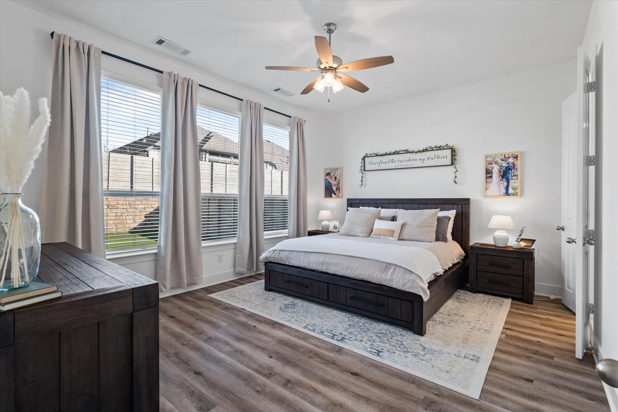 Wood-finish flooring, multiple windows, ceiling fan, white paneled door, and neutral wall tones