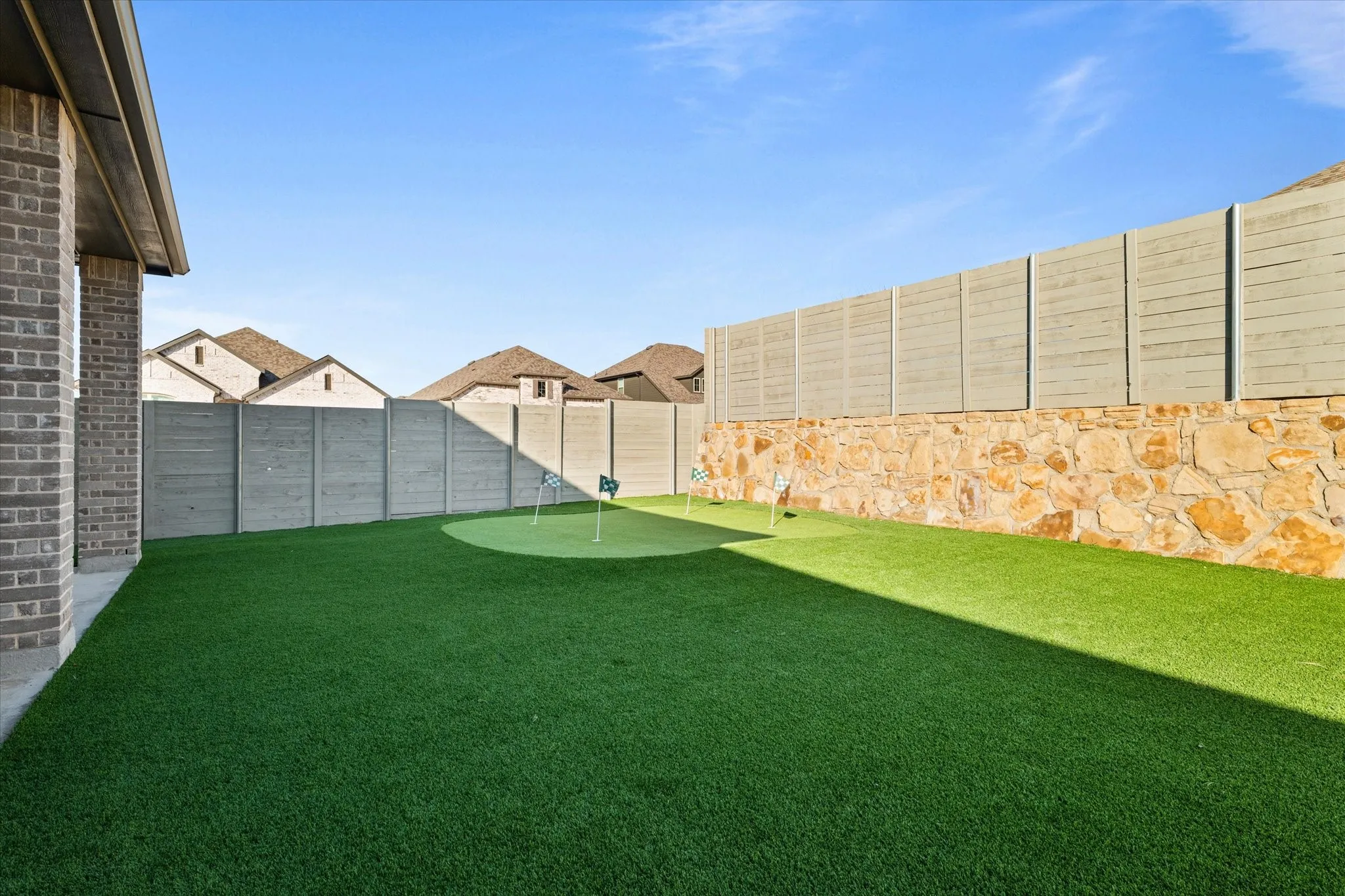 Expansive backyard with artificial turf, a built-in putting green, and a stone retaining wall