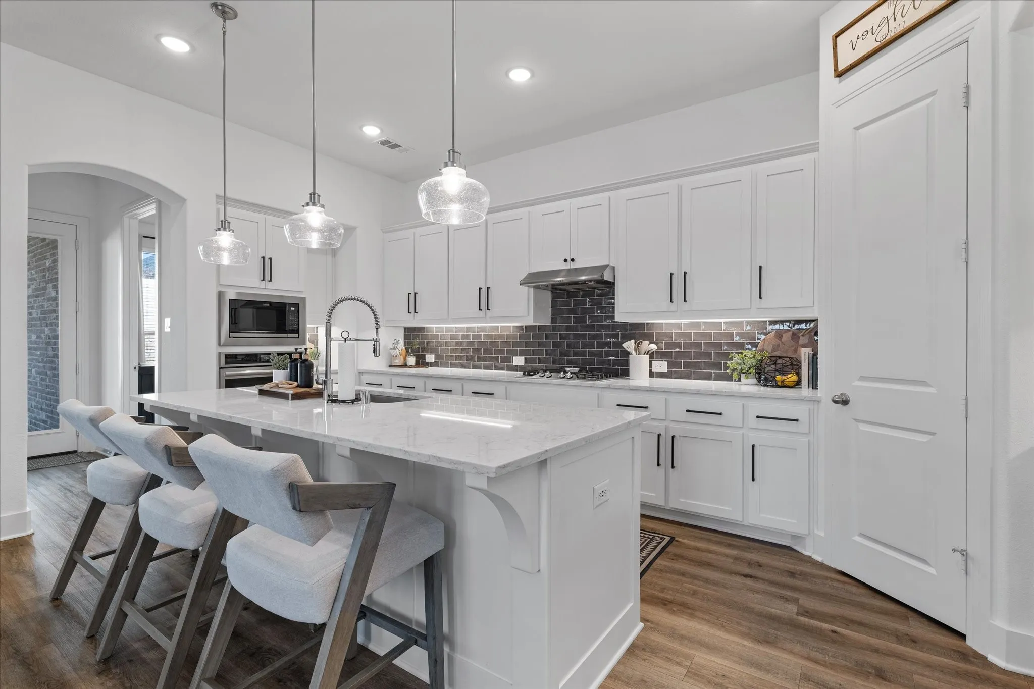 Kitchen featuring white cabinetry, a large central island with seating, stainless steel appliances, wood-finish flooring, and pendant lighting