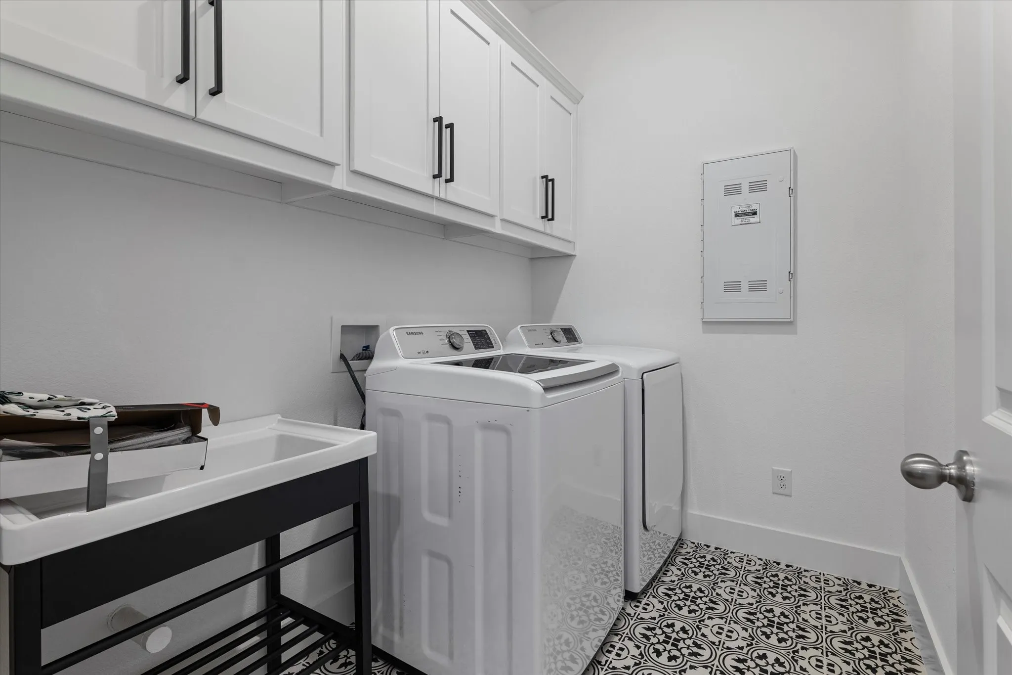 White shaker-style cabinetry with black hardware, patterned tile flooring, and utility sink