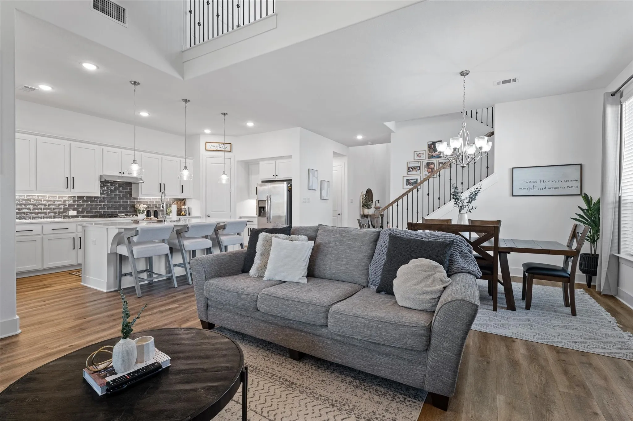 Open-concept living area featuring wood-finish flooring, a kitchen island with seating, pendant lighting, and an elegant staircase with dark balusters