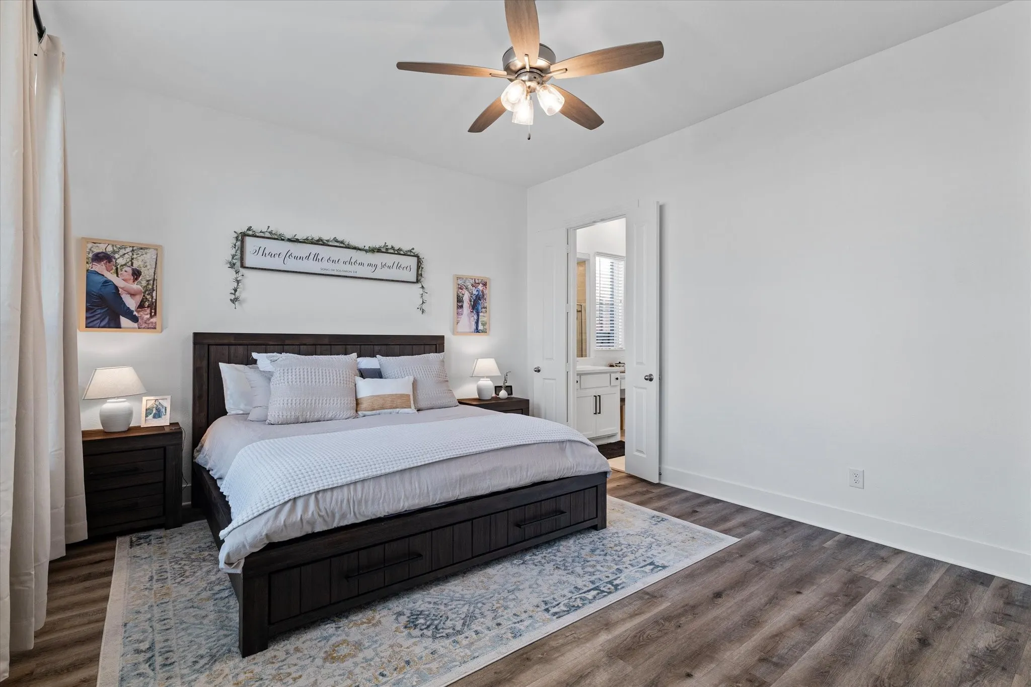 Spacious room featuring wood-finish flooring, a ceiling fan, and an open doorway revealing a bathroom with a vanity