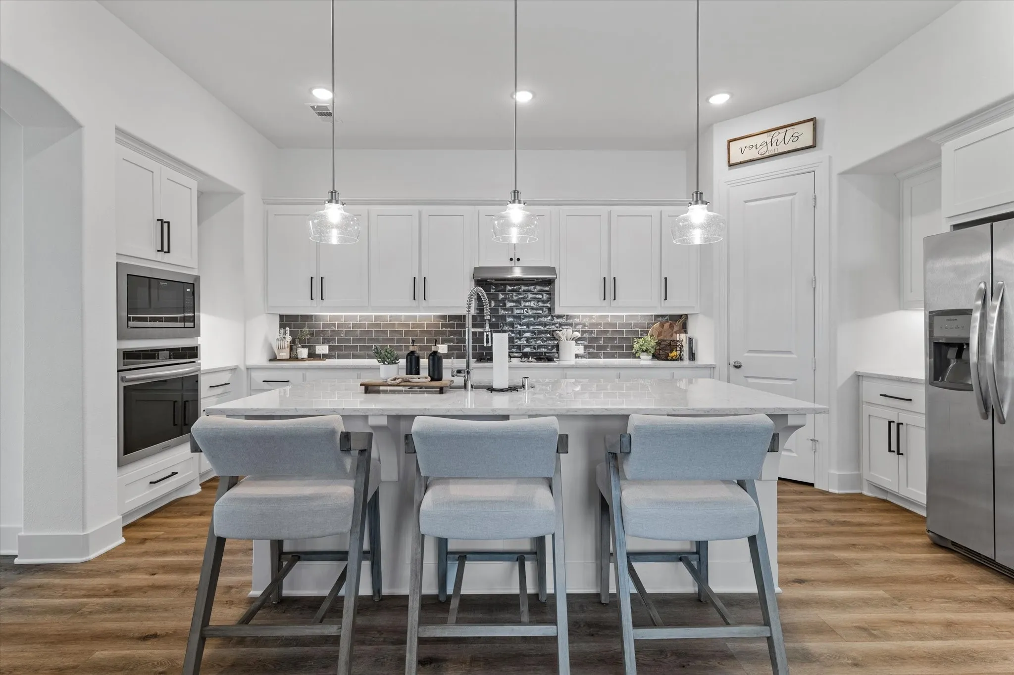 Gourmet kitchen featuring white cabinetry, stainless steel appliances, a large center island with a light-toned countertop, and wood-finish flooring